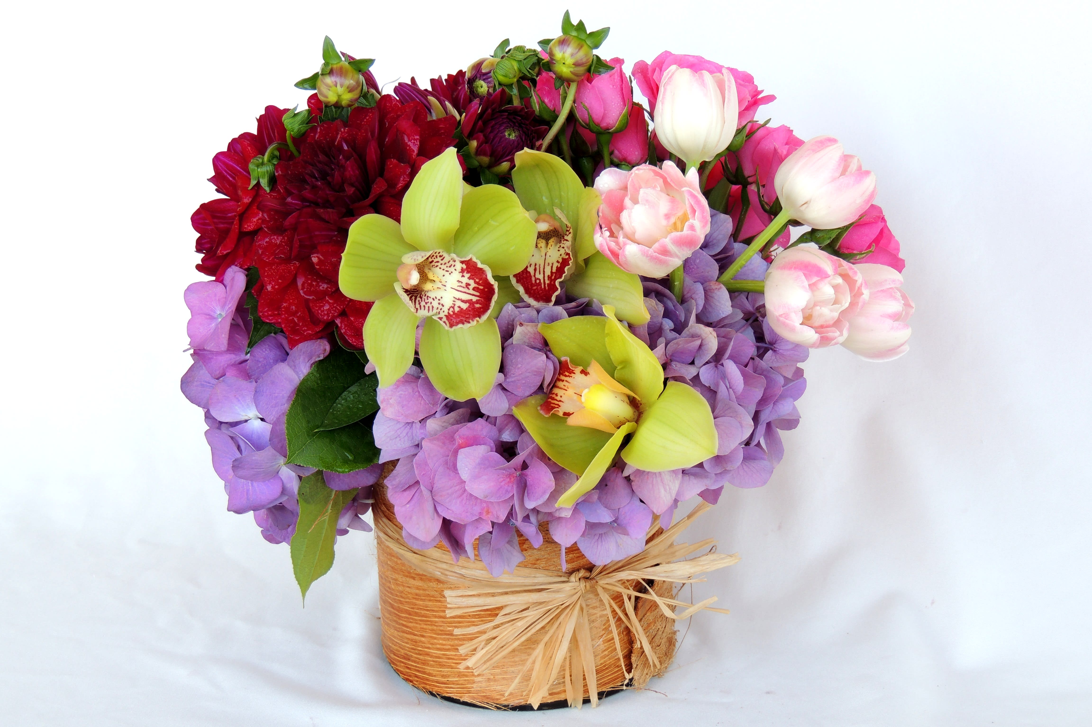 Dahlias in Spring  - Mix of dahlias, tulips, hydrangea, spray roses and orchids, in a cylinder containers lined with natural palm leaf. 