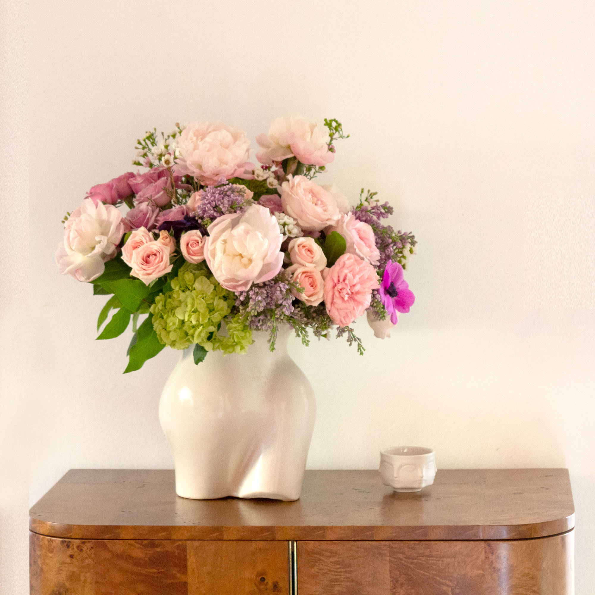 Mademoiselle - Pink and lavender blooms are a sweet and innocent way to show your affection. This arrangement features pink and lavender roses, lilacs, and pink peonies with a touch of green hydrangea in a vase that serves as an homage to the curves of the female form. Boasting a beautiful variety of flowers, this chic bouquet of feminine colors is full of texture and makes a fabulous gift.