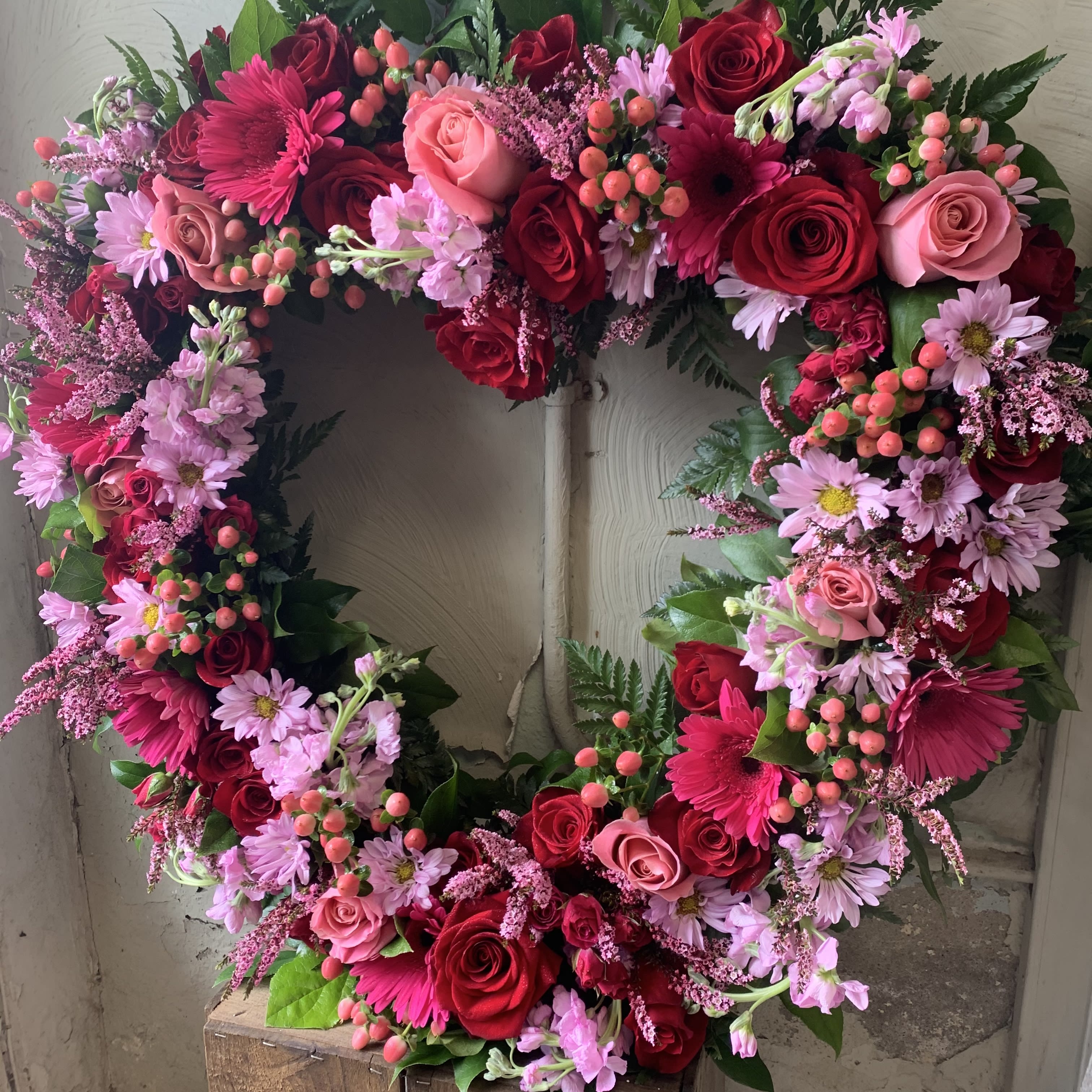 Eternal Open Heart -  Open Heart Easel in feminine pink and red tones. Includes premium roses, spray roses, gerber daisies, mini hydrangea, and other seasonal fresh flowers, arranged on an 18” open heart and displayed on an easel. (Deluxe approx 20” w X 24” h).
