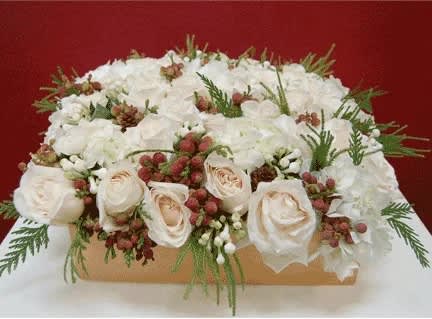 Dashing Through the Snow - A gorgeous mix of Imported White Roses and White Hydrangeas fill the base with beauty and grace. Artfully placed seasonal greens and red and white berries add holiday colors and Christmas flavor to this elegant design. Base Approx: 14&quot; W