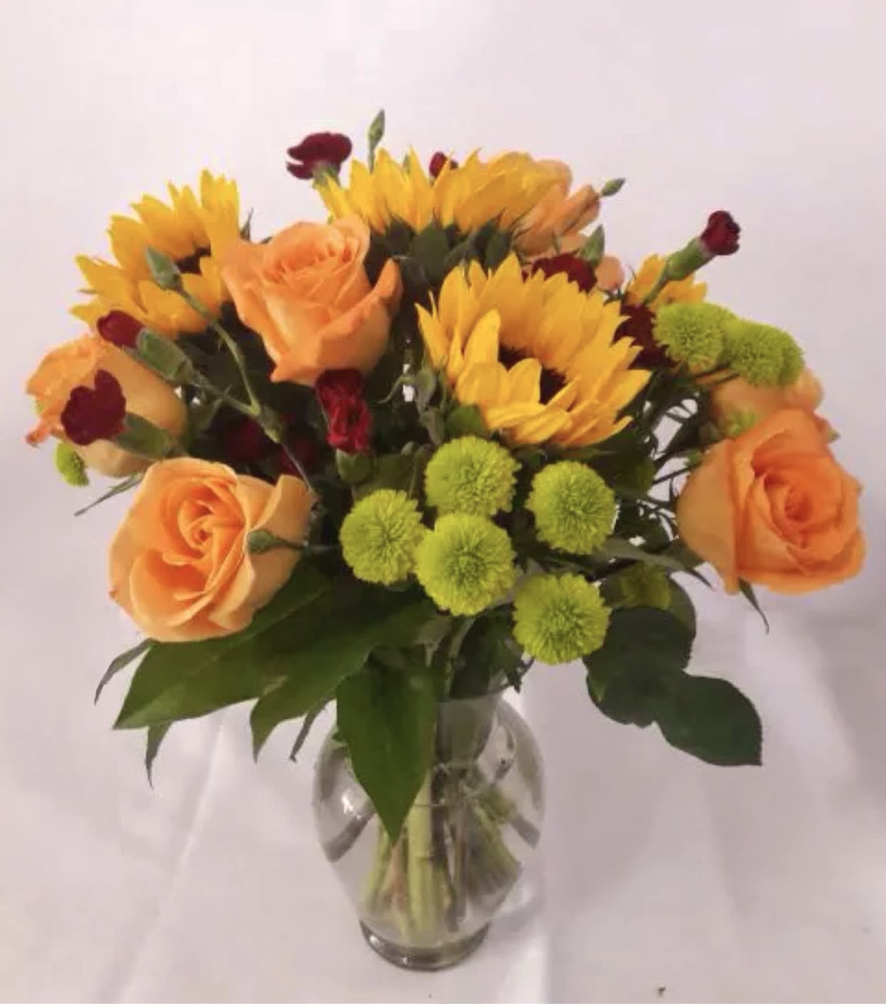 Blushing skies Blushing skies - Let your loved one know how much they mean to you with this beautiful arrangement that contains sunflowers, orange roses and green button poms in a clear vase.