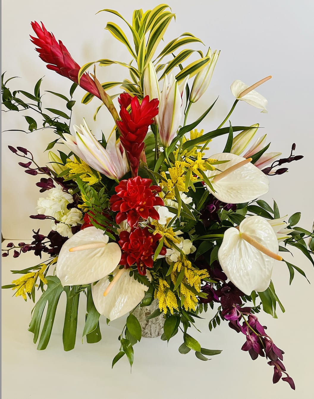 Tropical elegance - A combination of tropical foliage and tropical blooms. The perfect display for a special occasion.  Please contact us directly for any custom orders or requests info@helemelebotanicals.com or 808.226.7667.  We are committed to malama 'aina and strive to use locally sourced material, reduce packaging and reuse and recycle where possible. We will pick up any of our product (vessels, plants and floral supply material) when delivering a subsequent order. At that time, a $5 credit toward future purchase will be issued for each ceramic, metal or wood vessel returned.