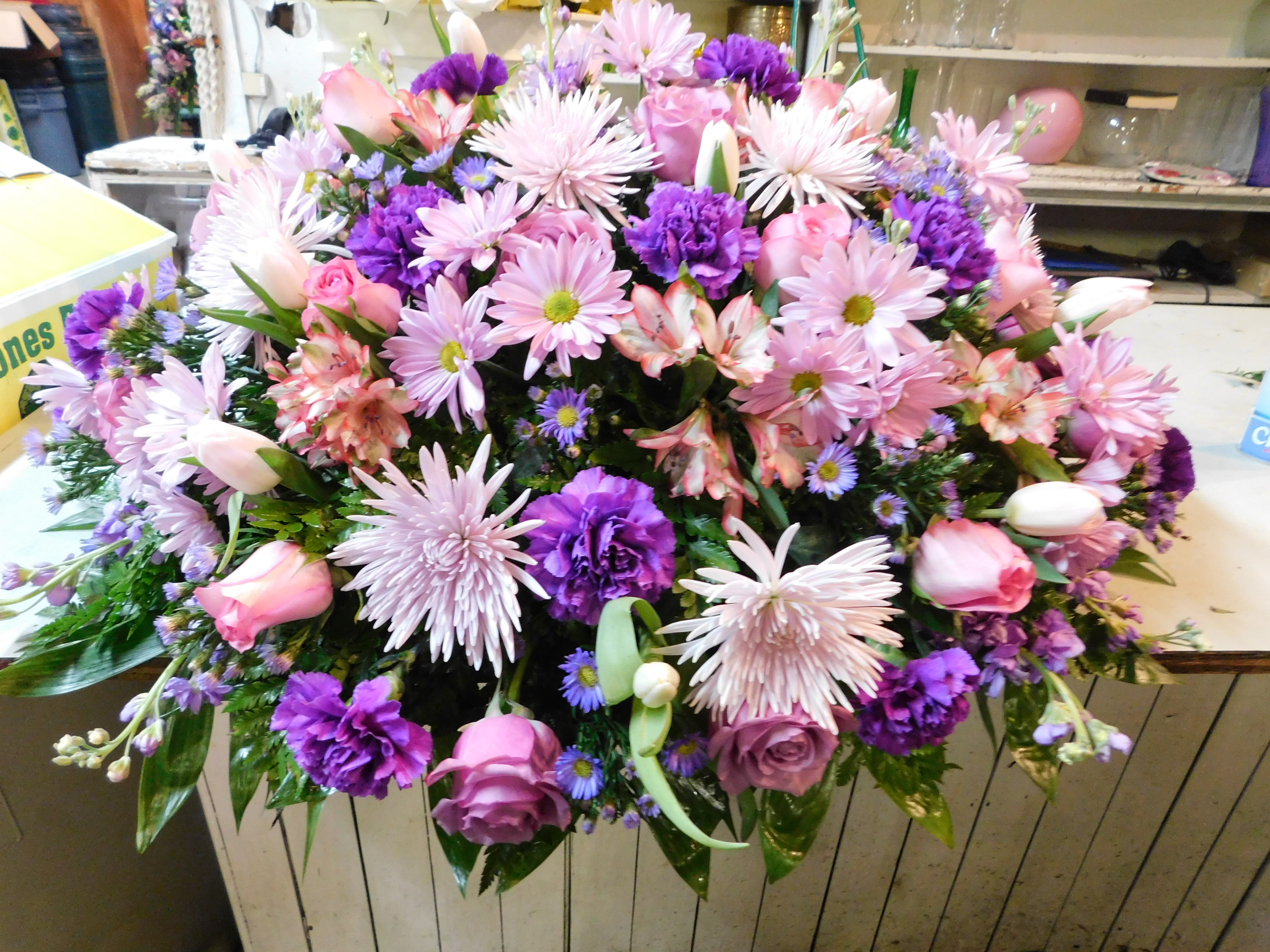 Pink and purple fushion - Lovely lavender and pink roses create this tribute that is overflowing with grace and love. Tulips, purple carnations, pink and lavender roses, white/pink tipped alstoemeria, and stock.
