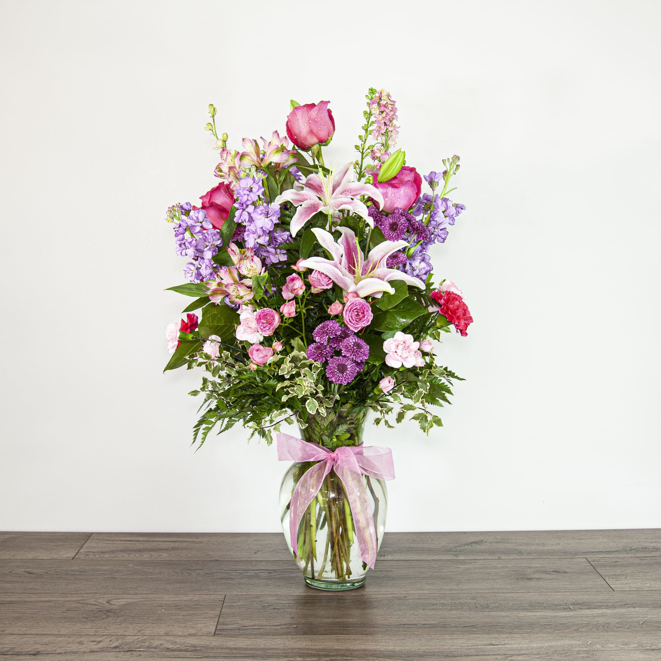 Extraordinarily Sweet (EXP 49-A) - Immerse yourself into the spring season with this large and full-of-life centerpiece, filled with pink and purple blooms. The look is finished off with a bow.  Blooms in this arrangement: -  hot pink spray rose stems -  sorbonne lilies -  pink alstromeria stems -  purple button pom stems -  hot pink carnations -  lavender stock -  pink larkspurs -  hot pink roses