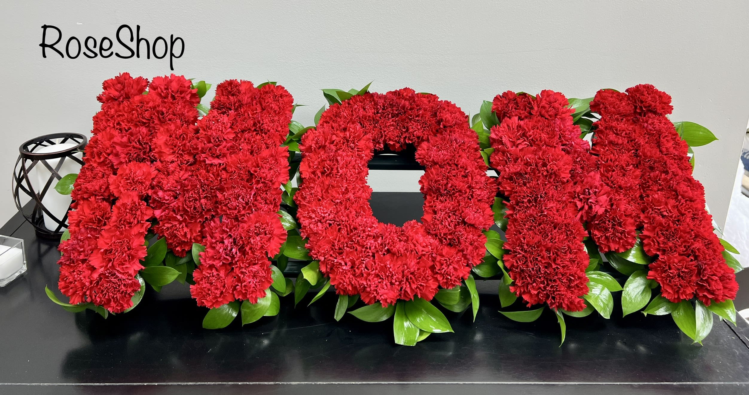 Mum Floral Tribute - Floral funeral letters spelling the word MUM. Based in all red carnations. Edged with green leaves.   Size: 29cm (11&quot;) height, 85cm (33.5&quot;) width approx.  