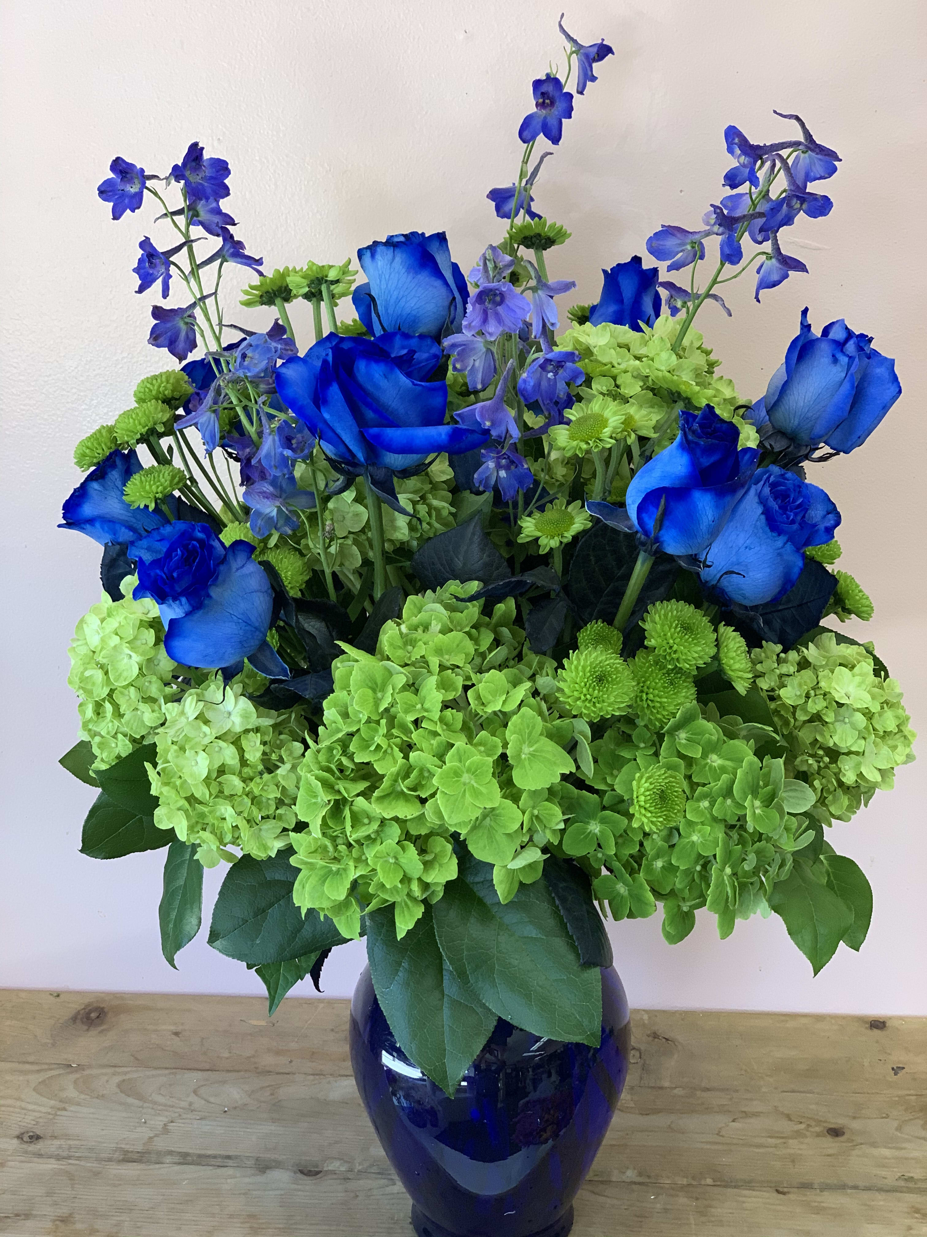 Green and Blue Floral - Green hydrangea, blue Bella Donna and blue roses arranged in blue glass vase. Dimensions approximately: 19”H-15”W