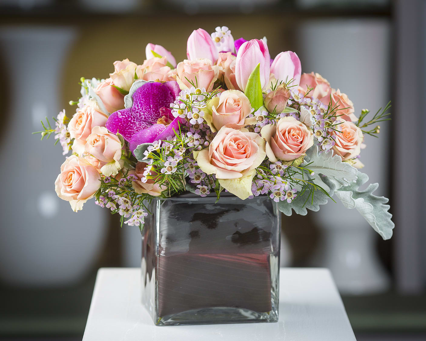 Dusty Peach - Spray roses, tulips, wax, dusty miller, &amp; vanda orchids in a leaf wrapped glass cube.