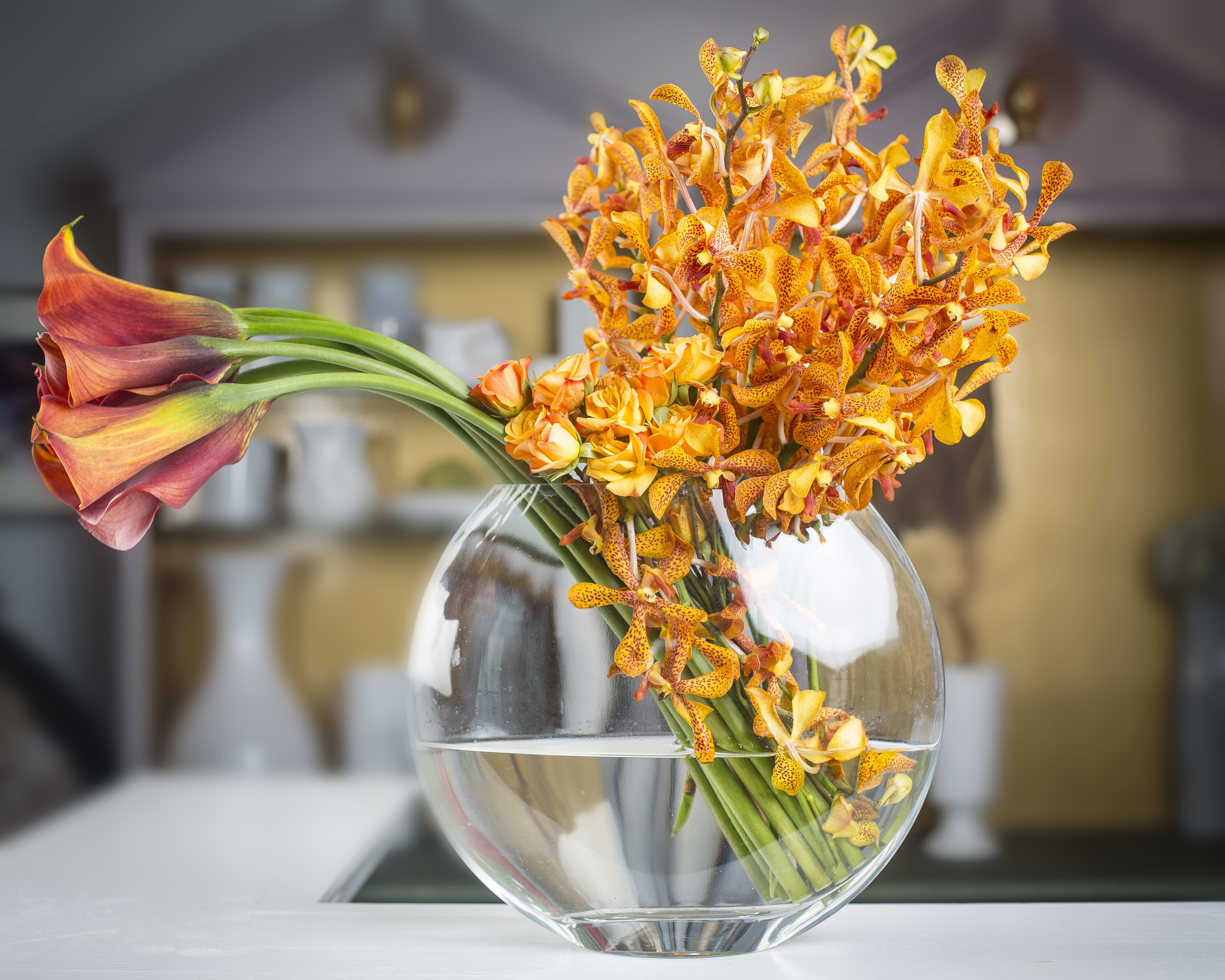 Mango Chanel - Mango calla lilies, spray roses &amp; mokara orchids in a round moon glass container.