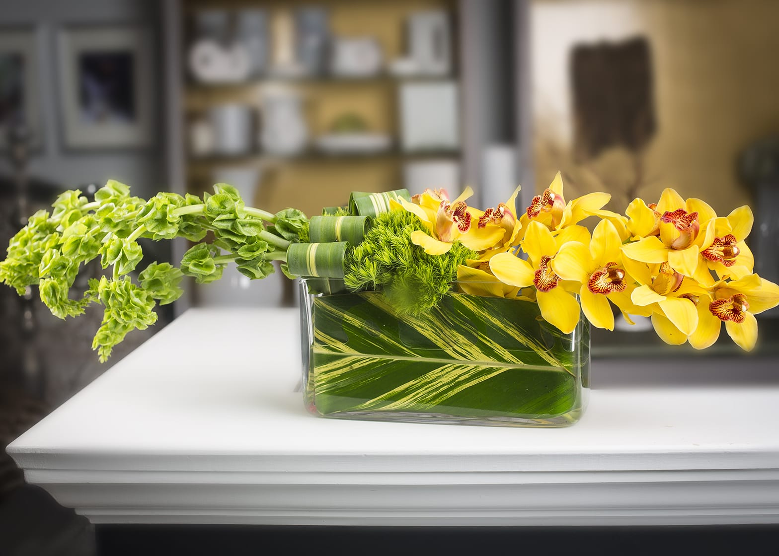 L &amp; L  - Cymbidium orchids, bells &amp; trick in a leaf wrapped glass rectangle container.