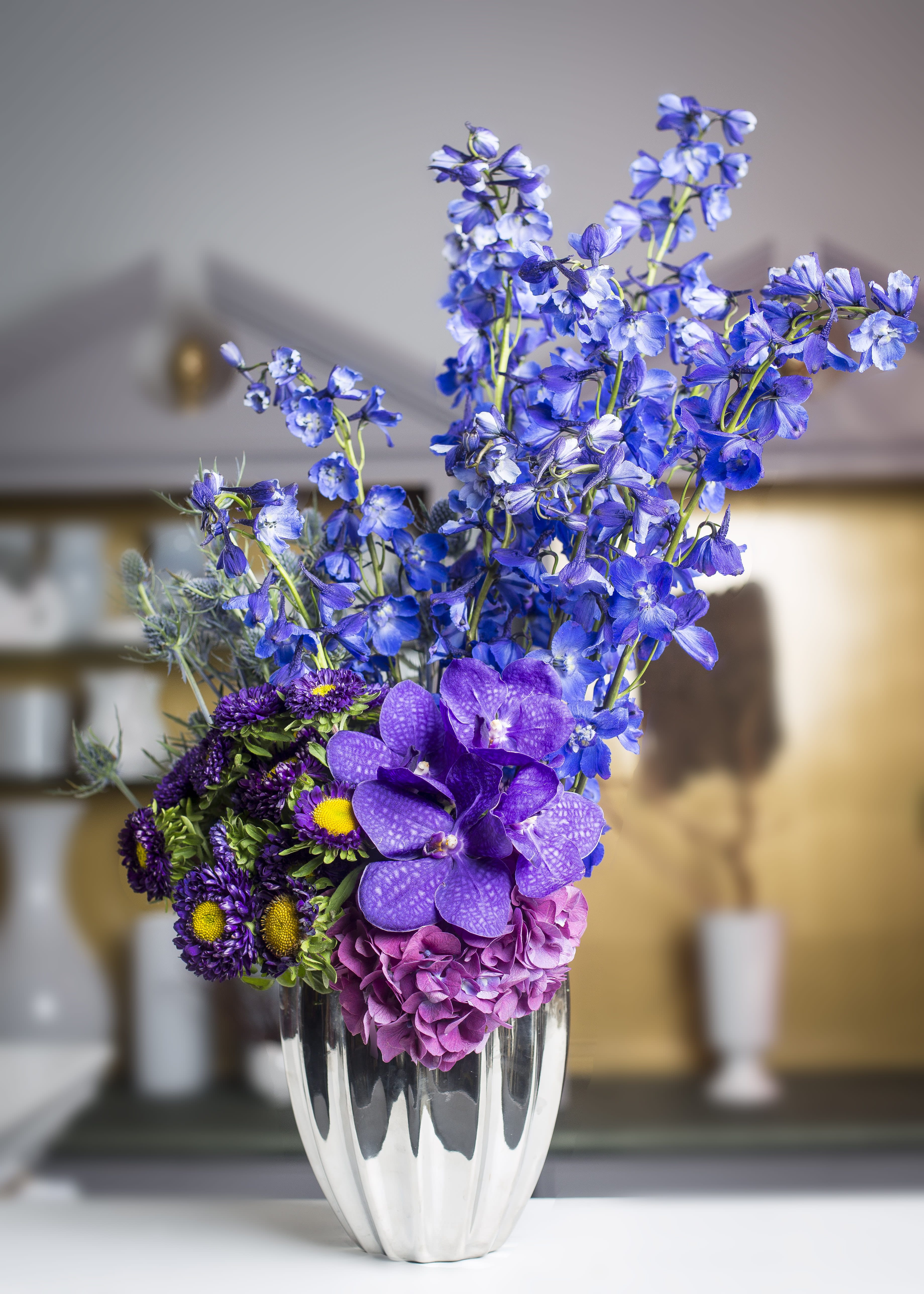 Designers Choice  - Beautiful hues of blue &amp; purple seasonal flowers in a round container- silver (default)  or your choice of black or white