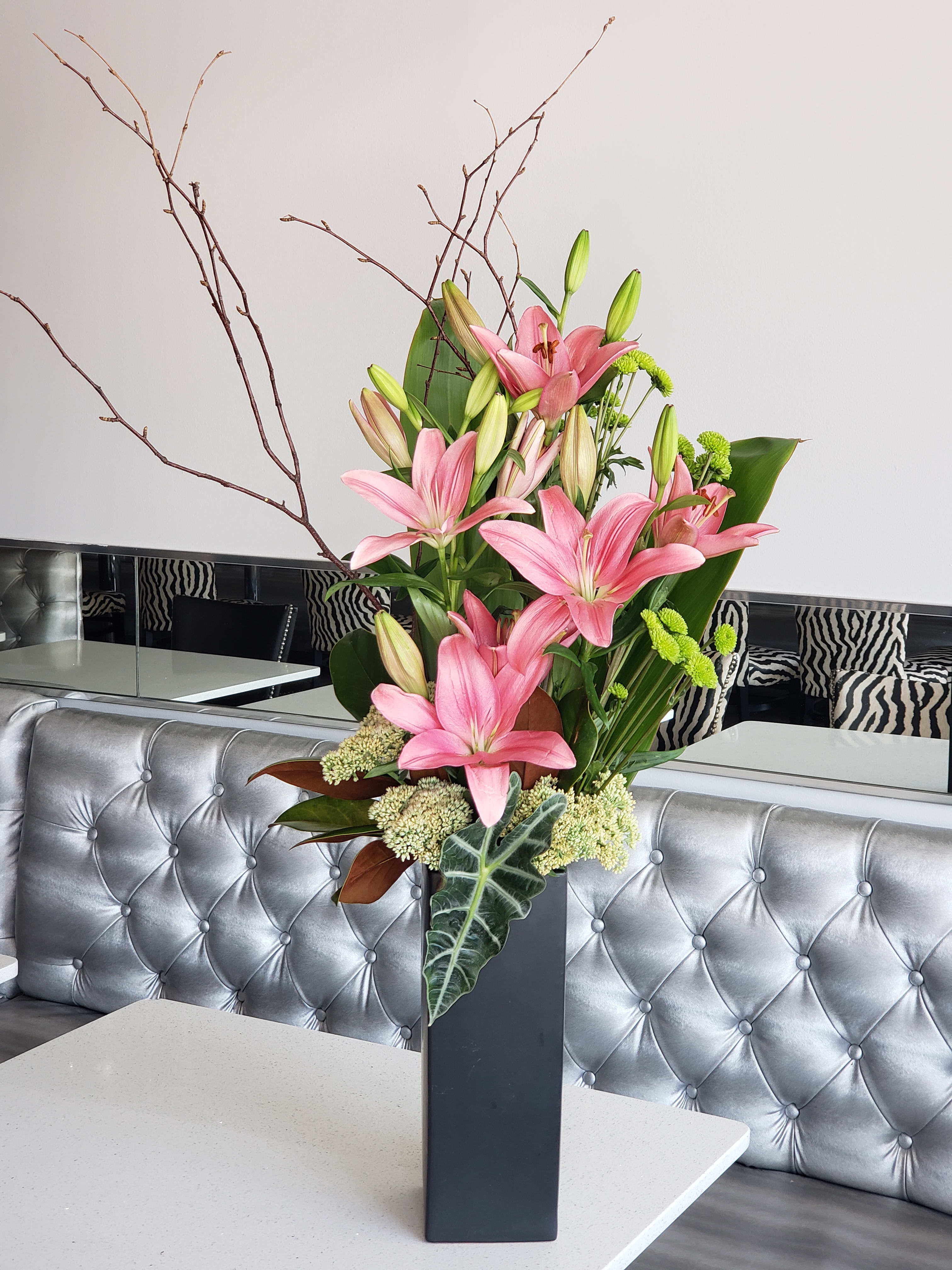 Pink Kitty - Pink lilies, kermit mums, ti leaves &amp; branches in a tall square container. 
