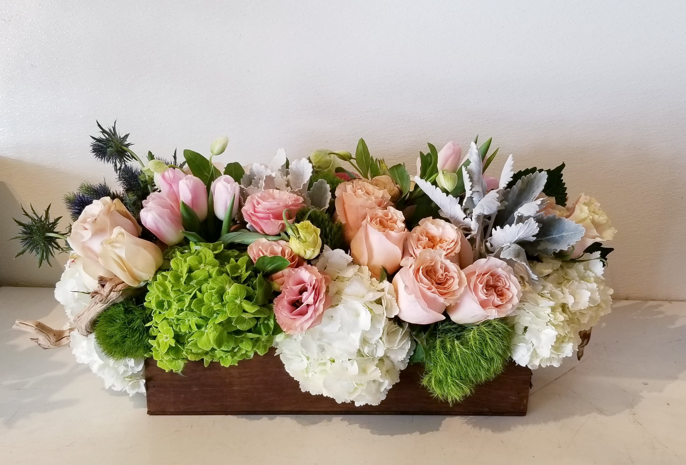 Bohemian Centerpiece - Long and low centerpiece in a brown wood box composed of neutral earthy tone floral blooms accented with driftwood branches. 