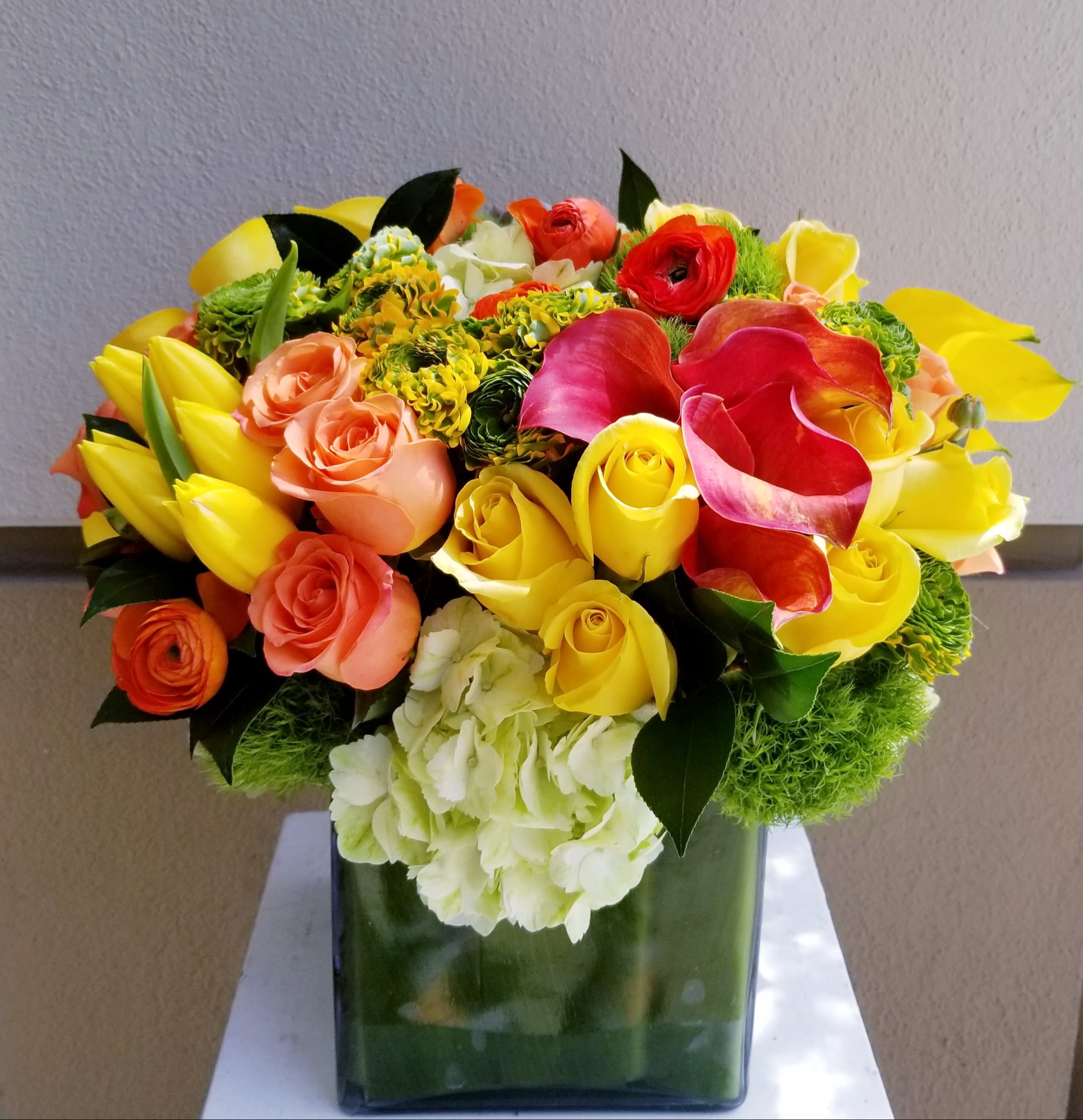 Citrus Blend - Bright yellow and orange blooms designed in a large square. Among the flowers used are mini calls, roses, tulips, ranunculus and hydrangeas.