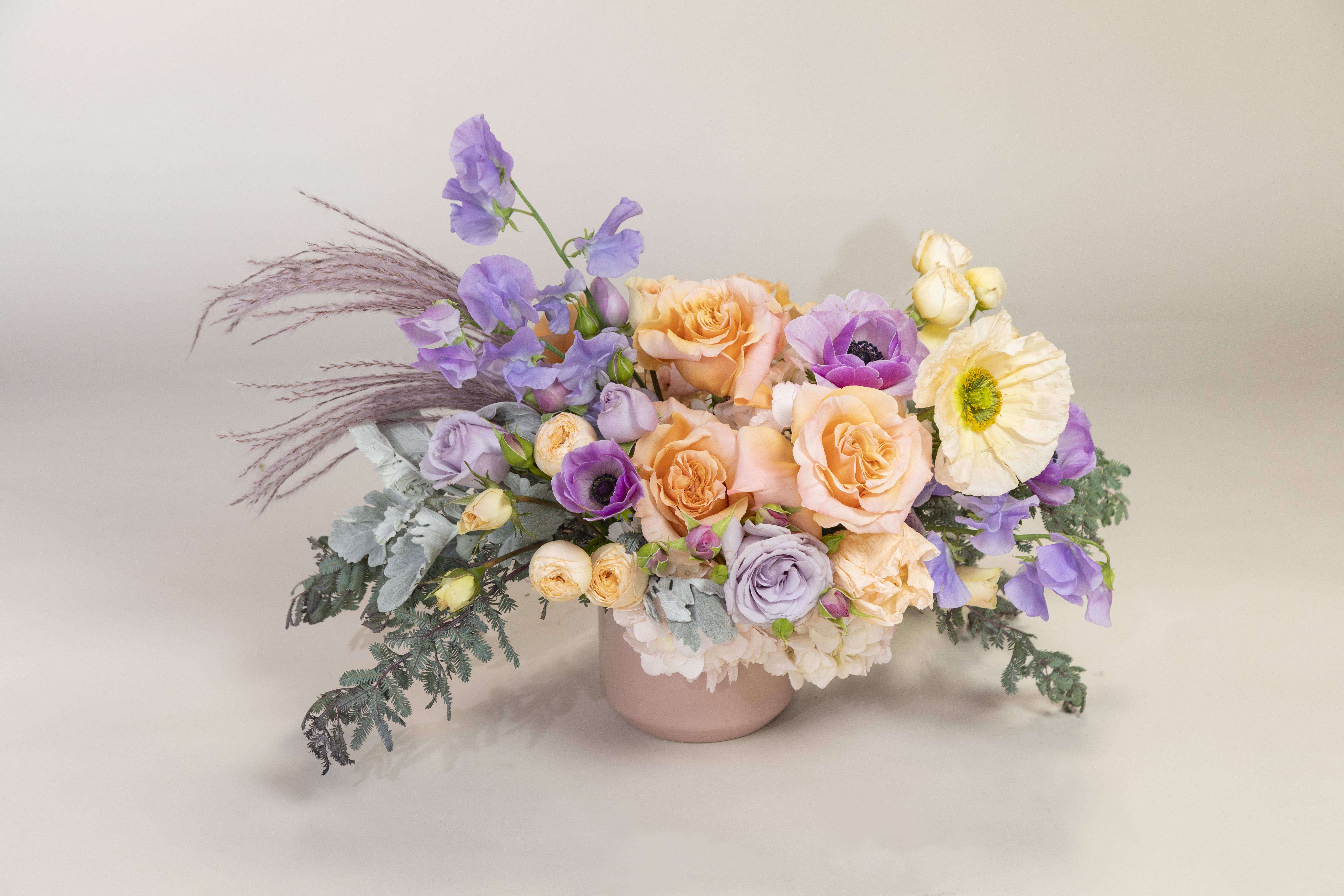 Juliet's Charm - This arrangement is filled with spring blooms including garden roses, poppies, sweet peas, anemones, and spray roses accented in soft colors of lavender and peach.