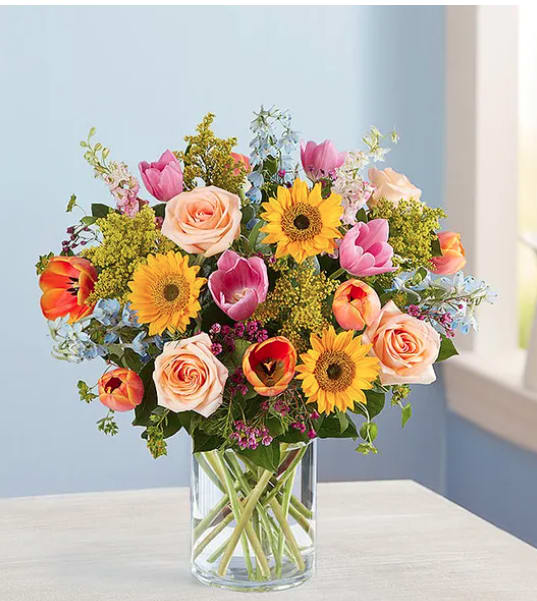 Vibrant Spring Sensation Vibrant Spring Sensation - There’s so much to love about spring…but it’s the bright, beautiful blooms that make it truly sensational! Our luxurious bouquet is gathered with a garden-fresh mix in shades of pink, blue, yellow and peach. Artistically designed, this gift delivers the best part of the season right to their door. All-around arrangement with peach roses, orange and pink tulips, mini sunflowers, pink larkspur and blue delphinium; accented with assorted greenery Artistically designed in a glass cylinder vase