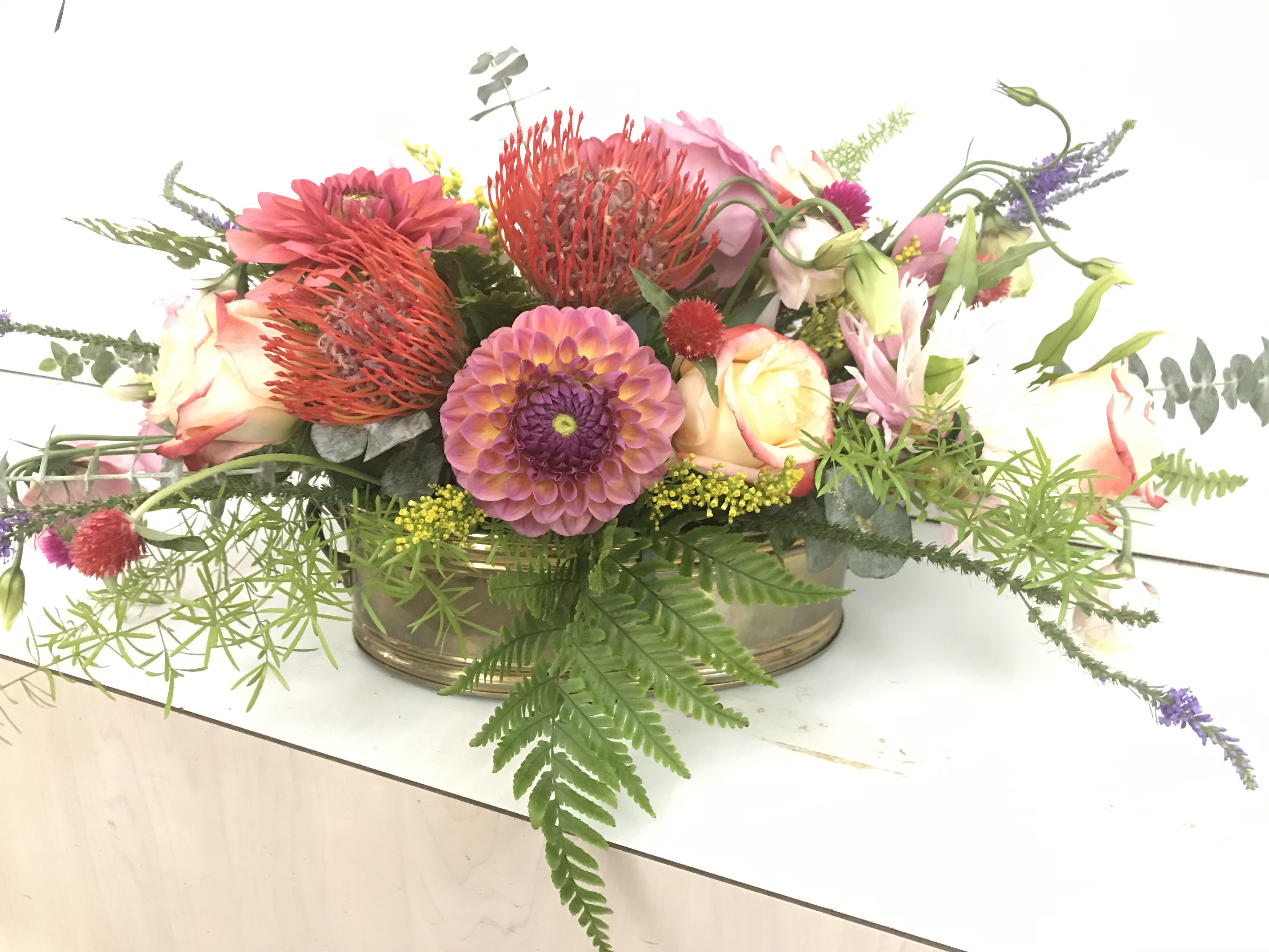 Simply Beautiful  - A beautiful low arrangement designed with a lovely mix of greens from our greenhouses and seasonal blooms, perfect for a dinner table or small table for a special event or occasion.