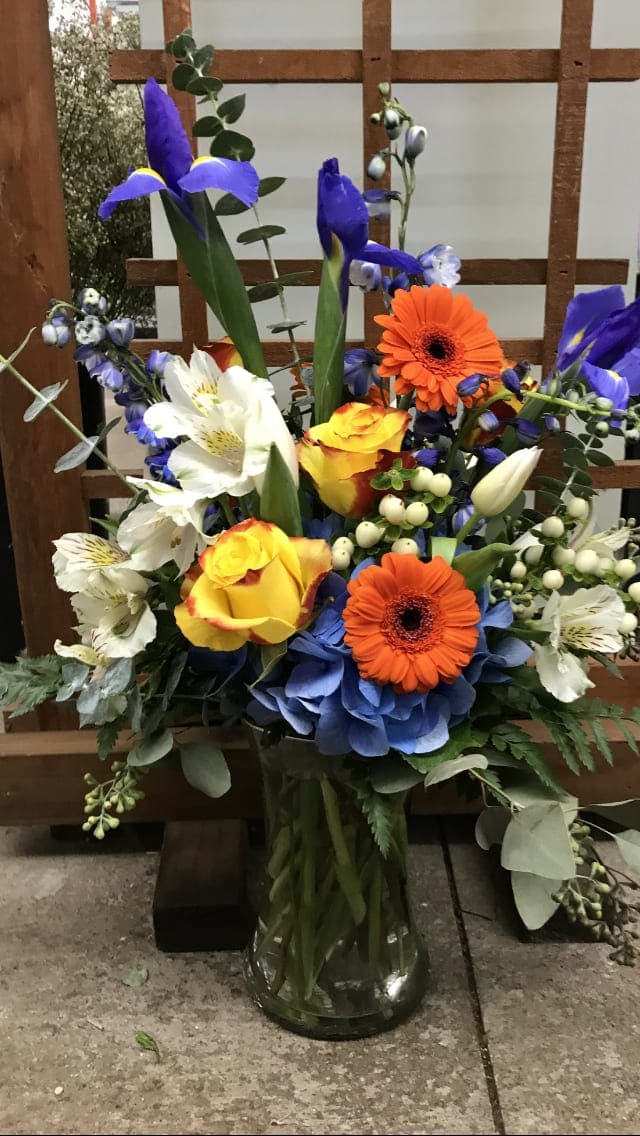 A Touch of Color. - A tall, bright design of seasonal blooms and greens, perfect to brighten a day.