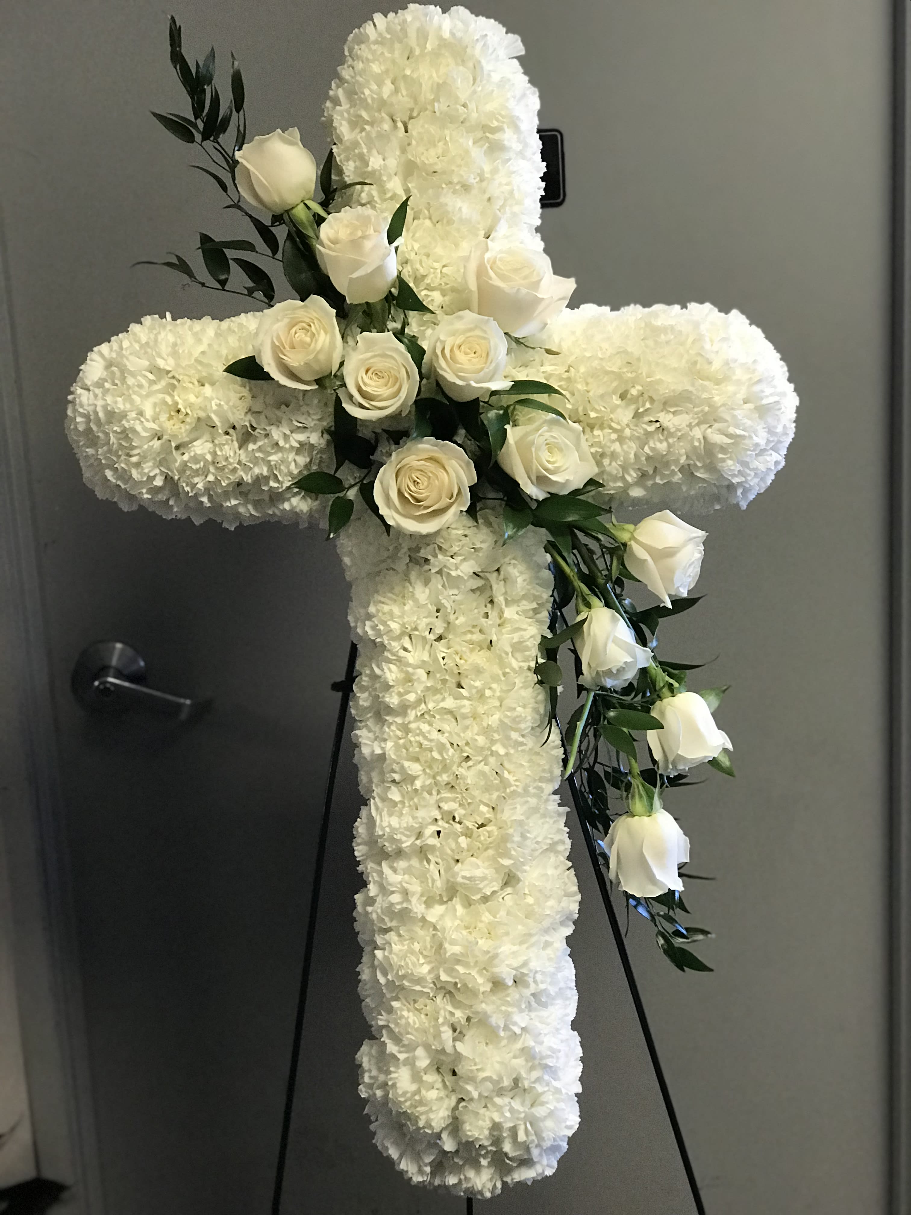  All White Cross -  White carnations are arranged in the shape of a cross accented in the middle with white roses and spray roses and along the sides with lush greens 