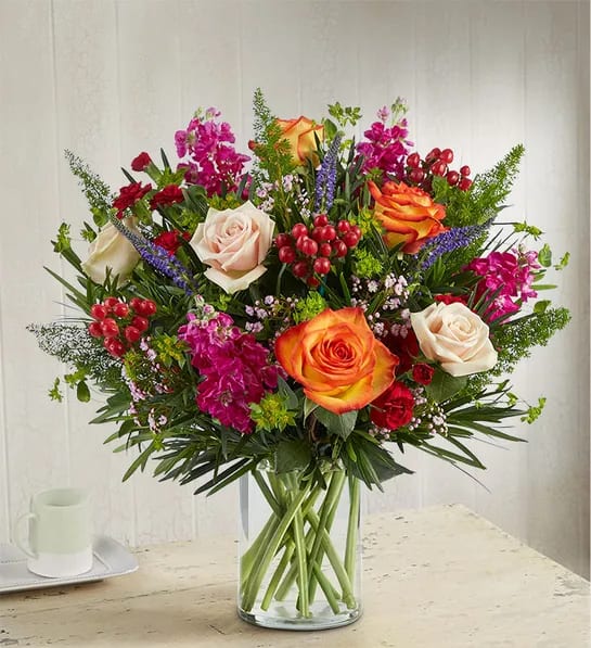 1800 Precious Gem™ Bouquet - Celebrate a precious gem in your life. Our garden-inspired arrangement is gathered with a unique variety of jewel-tone blooms and lush greenery. Designed in a clear glass vase to that, it’s a gift that sparkles as bright as they do.  All-around arrangement with purple Veronica, cream and orange bi-color roses, burgundy mini carnations and hypericum, fuchsia stock, pink waxflower; accented with assorted, unique greenery Artistically designed in a clear glass cylinder vase; measures 8&quot;H Large arrangement measures approximately 27&quot;H x 24&quot;W Medium arrangement measures approximately 24&quot;H x 21&quot;W Small arrangement measures approximately 23&quot;H x 20&quot;W Our florists hand-design each arrangement, so colors, varieties and container may vary due to local availability