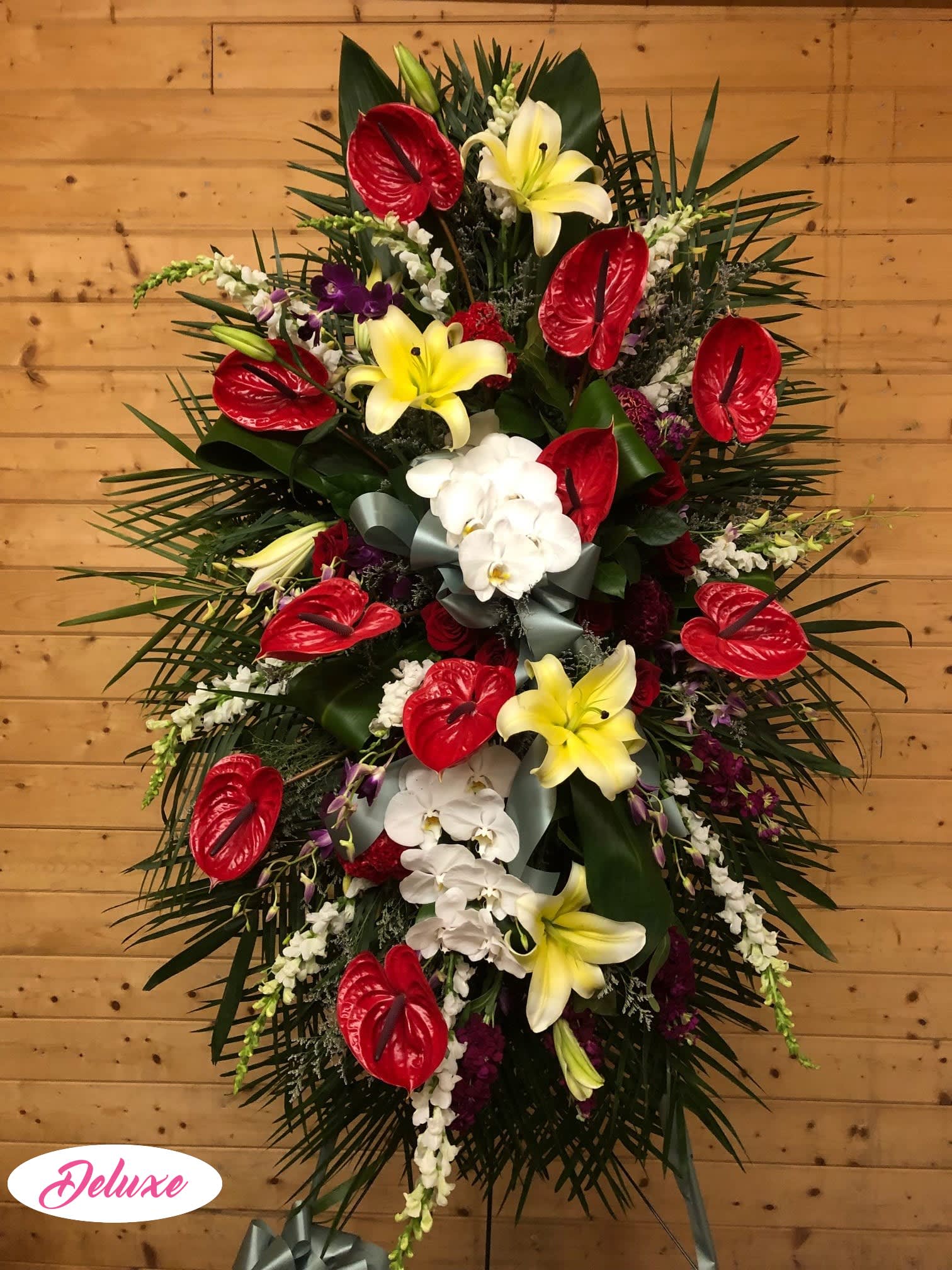 Tropical Standing Spray Tropical Standing Spray - Red anthurium, orchids, roses, lilies, curly willow are arranged with mixed greens. Delivered on an easel, this one-sided design is suitable to send to the funeral home or service.