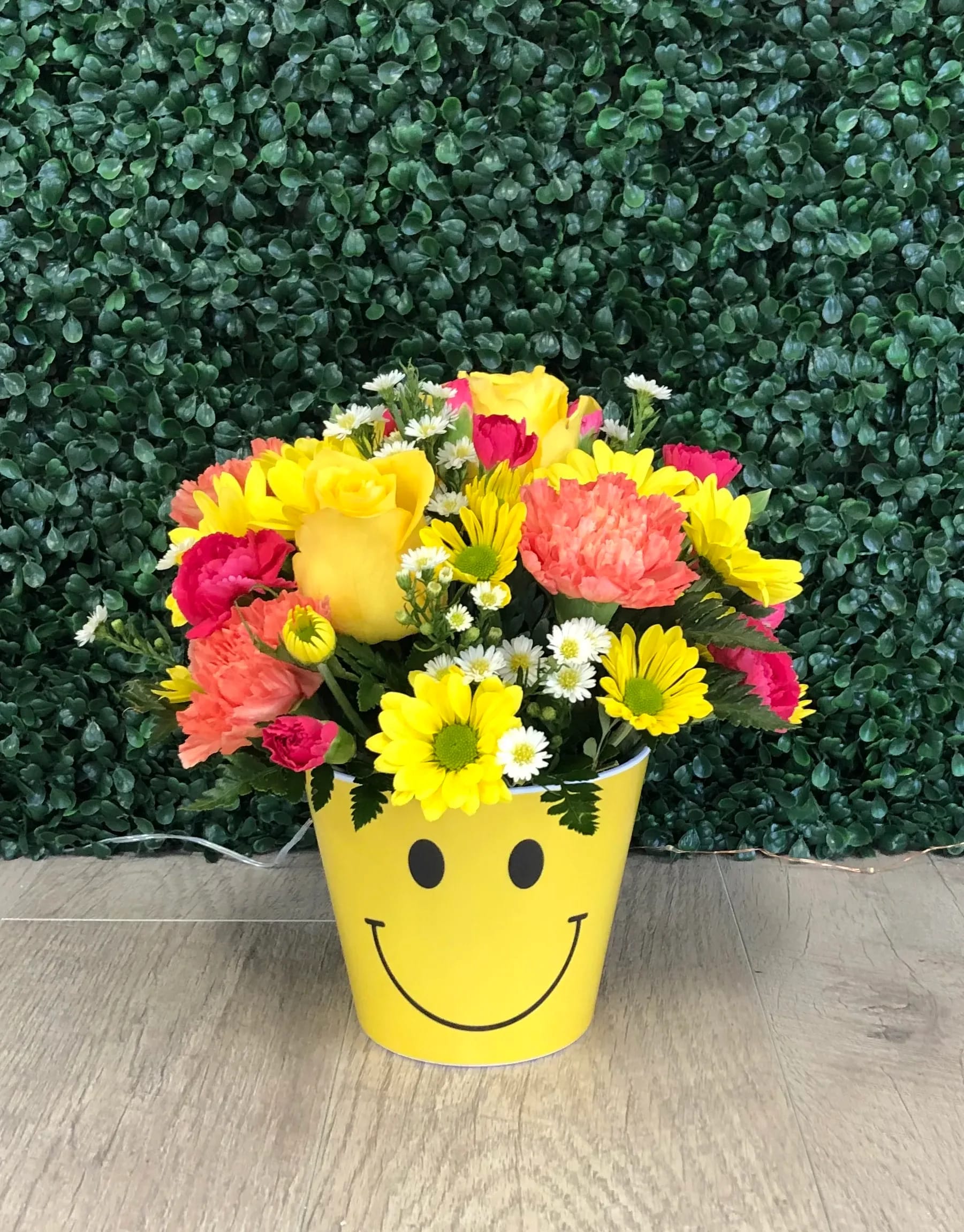 Smiles Bouquet - Ruth Mesmer Florist Smiles Bouquet is a perfect way to make any one smile and feel happy. The ceramic smiley container is designed with yellow roses, orange carnations, yellow daisies and hot pink mini carnations. Apprx 10&quot; tall by 10&quot; wide