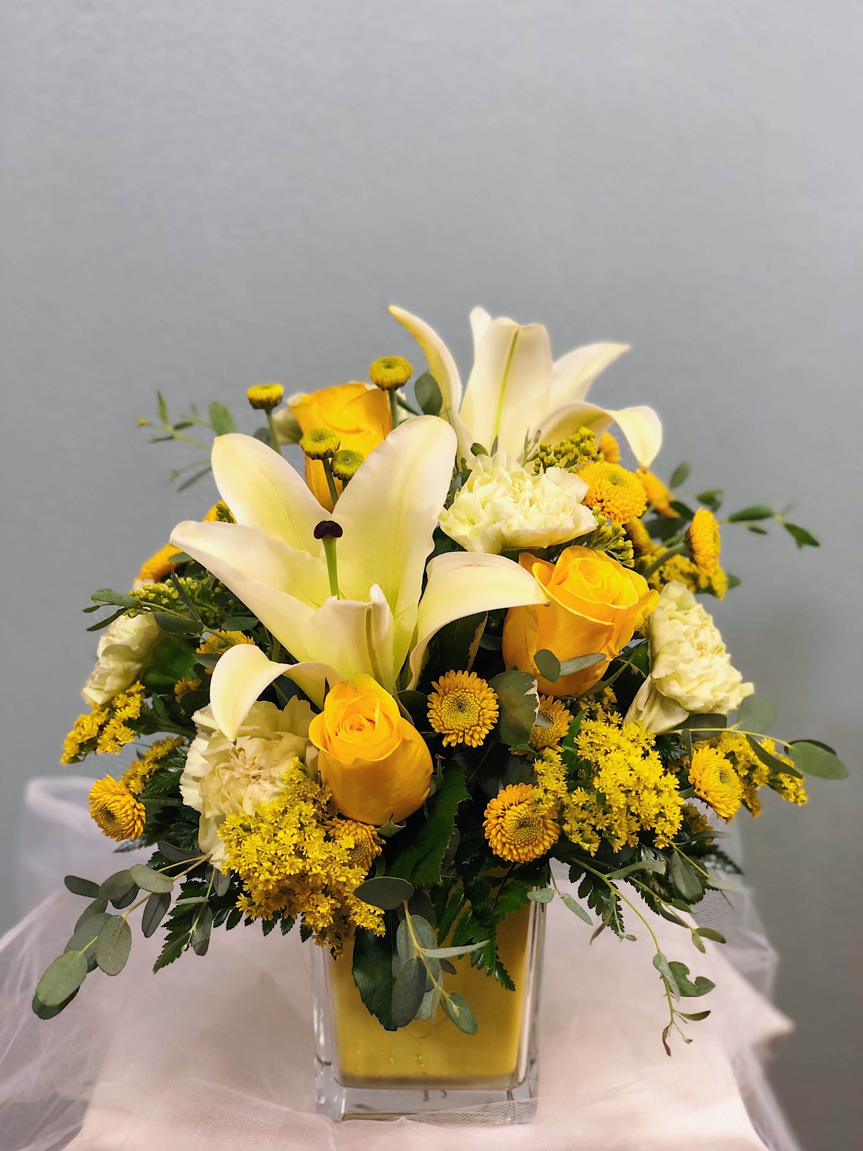 Happy and Yellow  - Happy and Yellow describes this arrangement perfectly! This will be sure to brighten even the gloomiest day! Happy and Yellow is a mixture of all flowers yellow! Two pale yellow lilies take center stage surrounded by three bright yellow roses, four pale yellow carnations, and yellow buttons and solidago for accent flowers. Sprigs of gunni eucalyptus and green leather leaf fill out the arrangement. Happy and Yellow even comes designed in a yellow keepsake cube! 