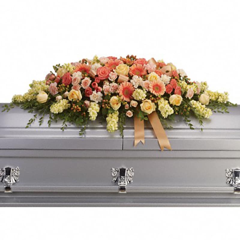 Warmest Remembrance Casket Spray [T266-3A] - This tastefully colorful casket spray is not only a tribute to a lost loved one, but a reminder of the many joyous times spent together.  The beautiful bouquet includes peach roses, light pink spray roses, coral spray roses, light orange gerberas, light orange carnations, light yellow stock and peach hypericum, accented with satin ribbon and assorted greenery.  Approximately 50&quot; W x 17 1/2&quot; H  Orientation: N/A  As Shown : T266-3A