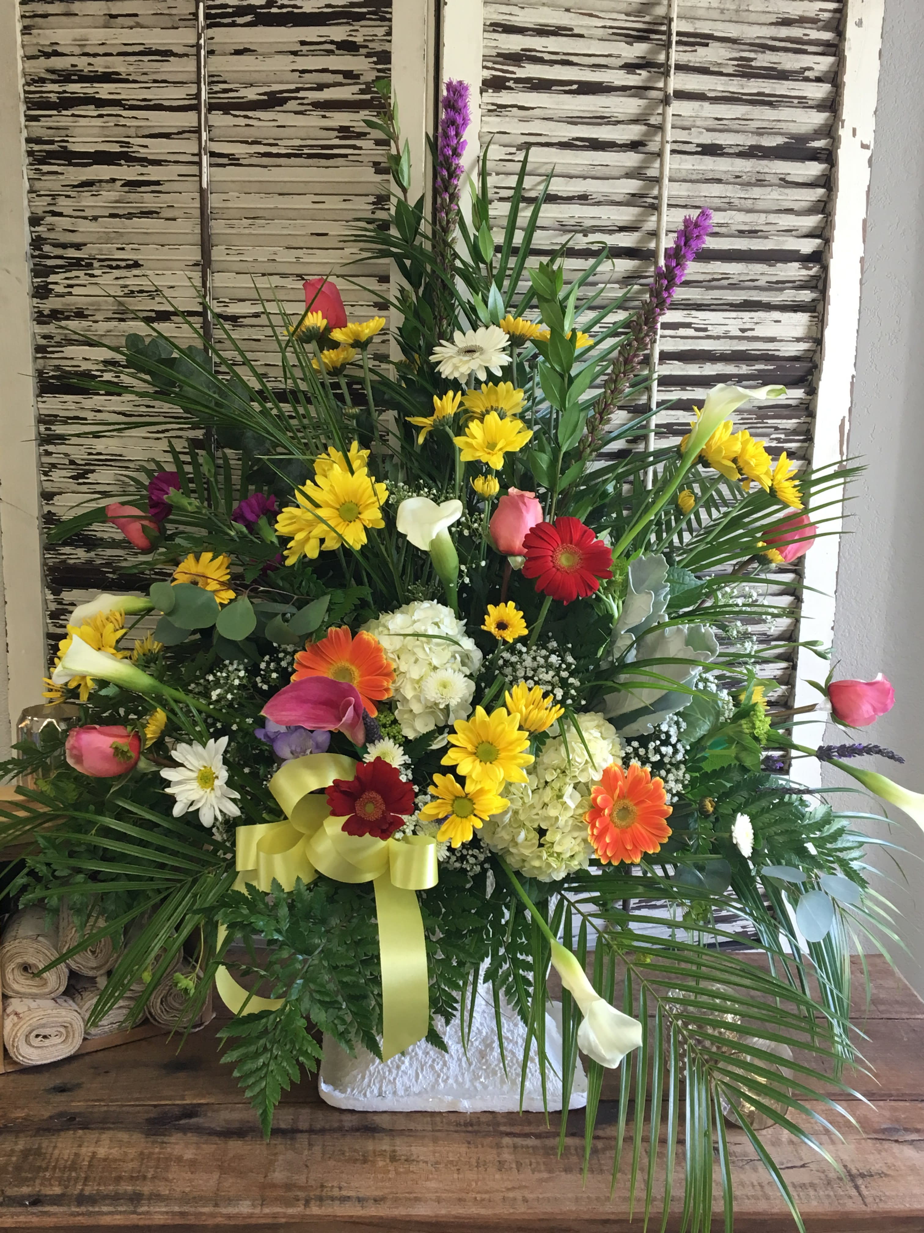Loving Tributes Loving Tributes - A beautiful One Sided Arrangement in bright colors. Arrangement is filled with MIni Calla Lillies, Gerbera Dasies, Roses, Liatris, Hydrangea and Daisies all arranged in a white container. Substitutions are possible but we do our best to stay in same color scheme.