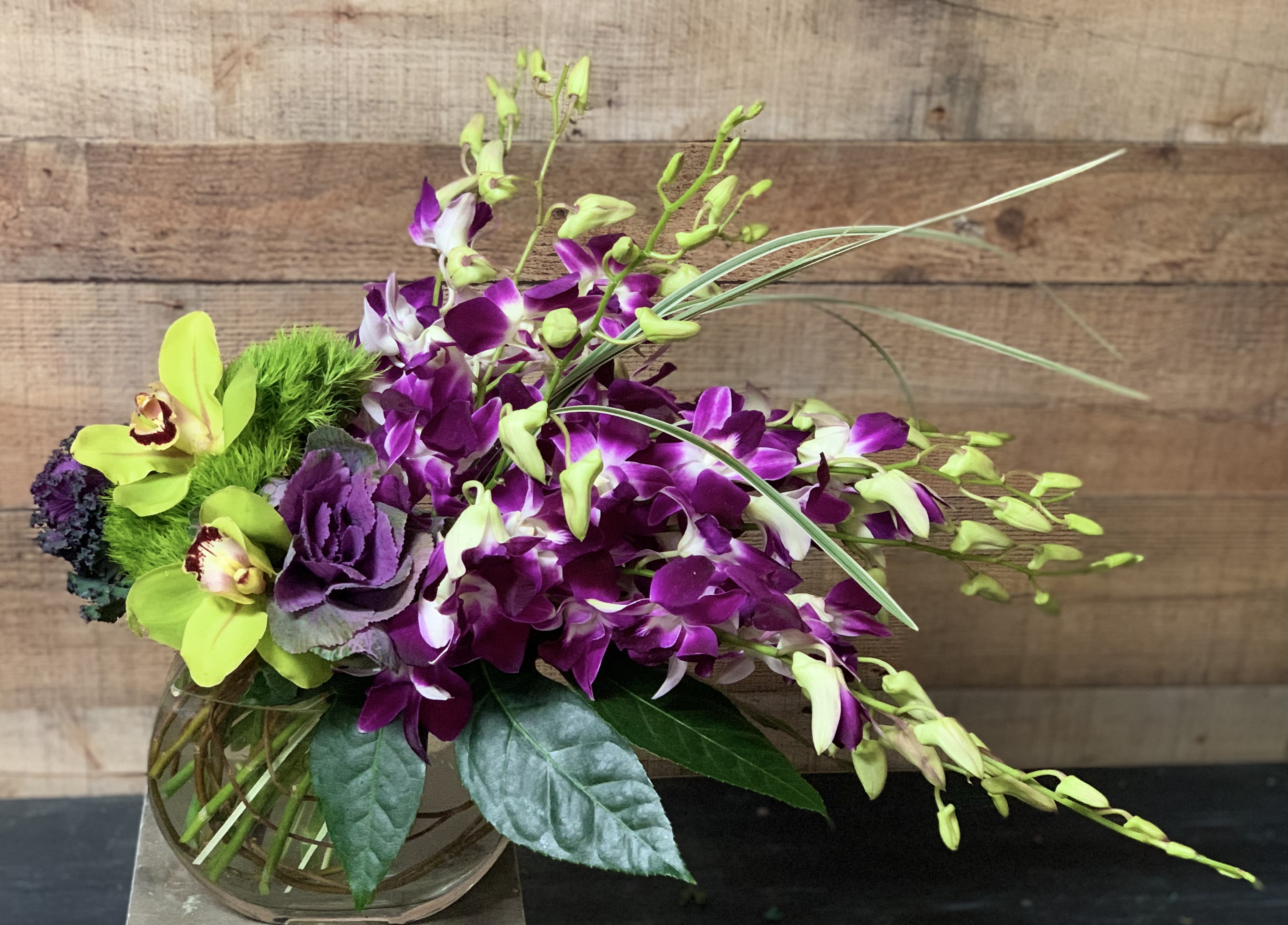 Lovely Orchids - Dendrobium and cymbidium orchids along with kale artistically designed in a clear glass vase