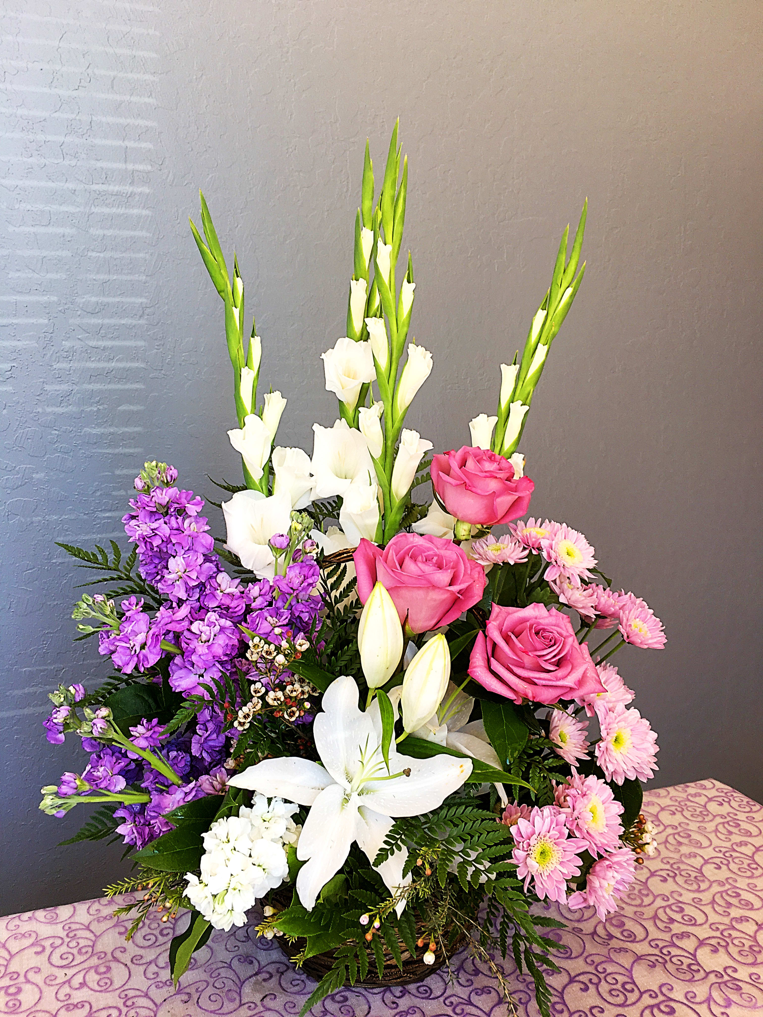FB#01 Memories Lavender Basket - This unique sympathy basket accents white lilies, white gladiolus, purple roses, lavender pompom and lavender stocks with greens and ferns.  Orientation: One-Sided  The arrangement is approximately 24&quot; H and 18&quot; W.
