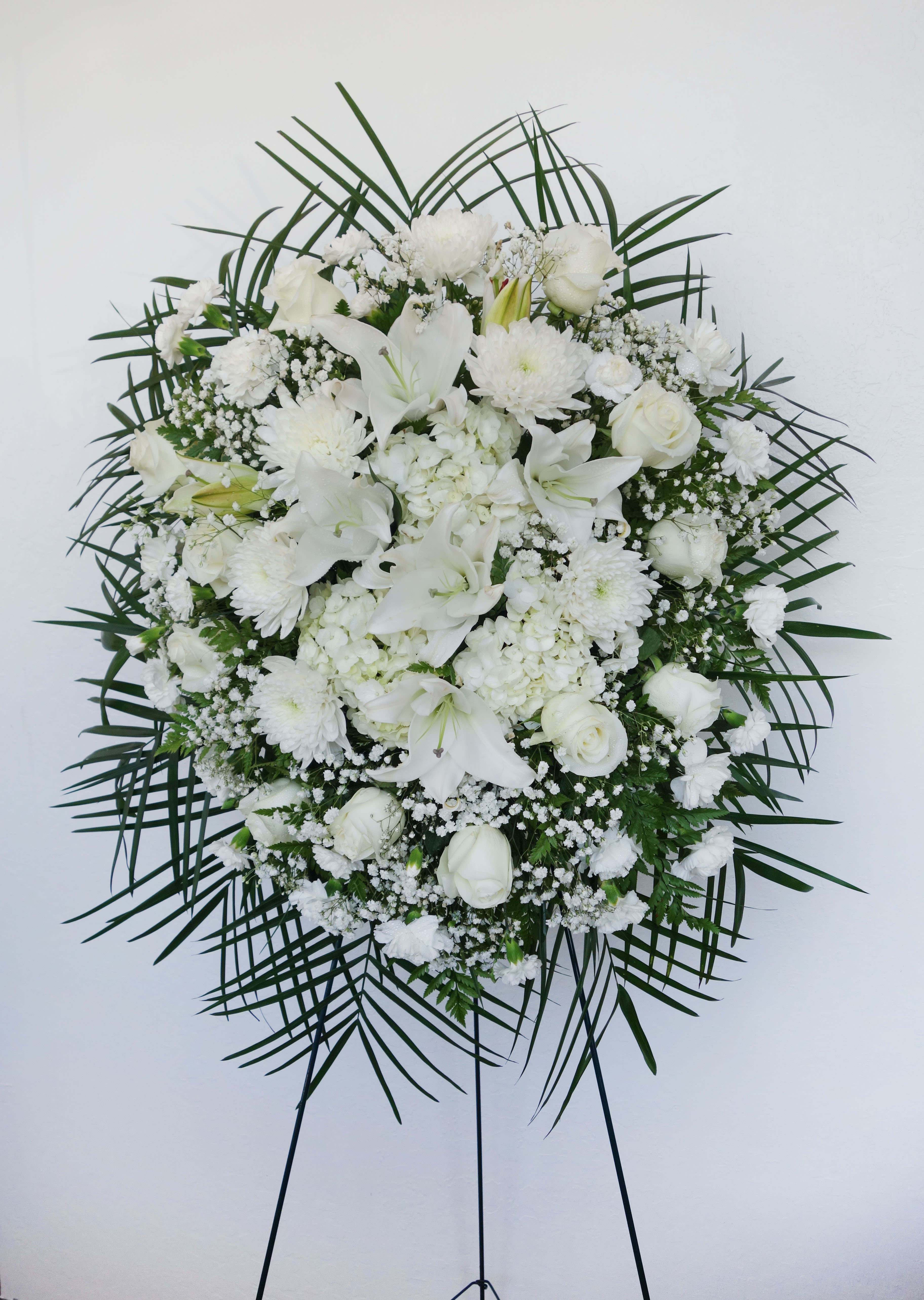 SS#15 White Purity Spray - A sign of purity with all white flowers in a rounded arrangement style, a soft and simple standing spray. This standing spray features lilies, roses, hydrangeas, football mums, carnations, baby's breath, and mixed foliage.  The arrangement is approximately 48&quot; H and 24&quot; W.