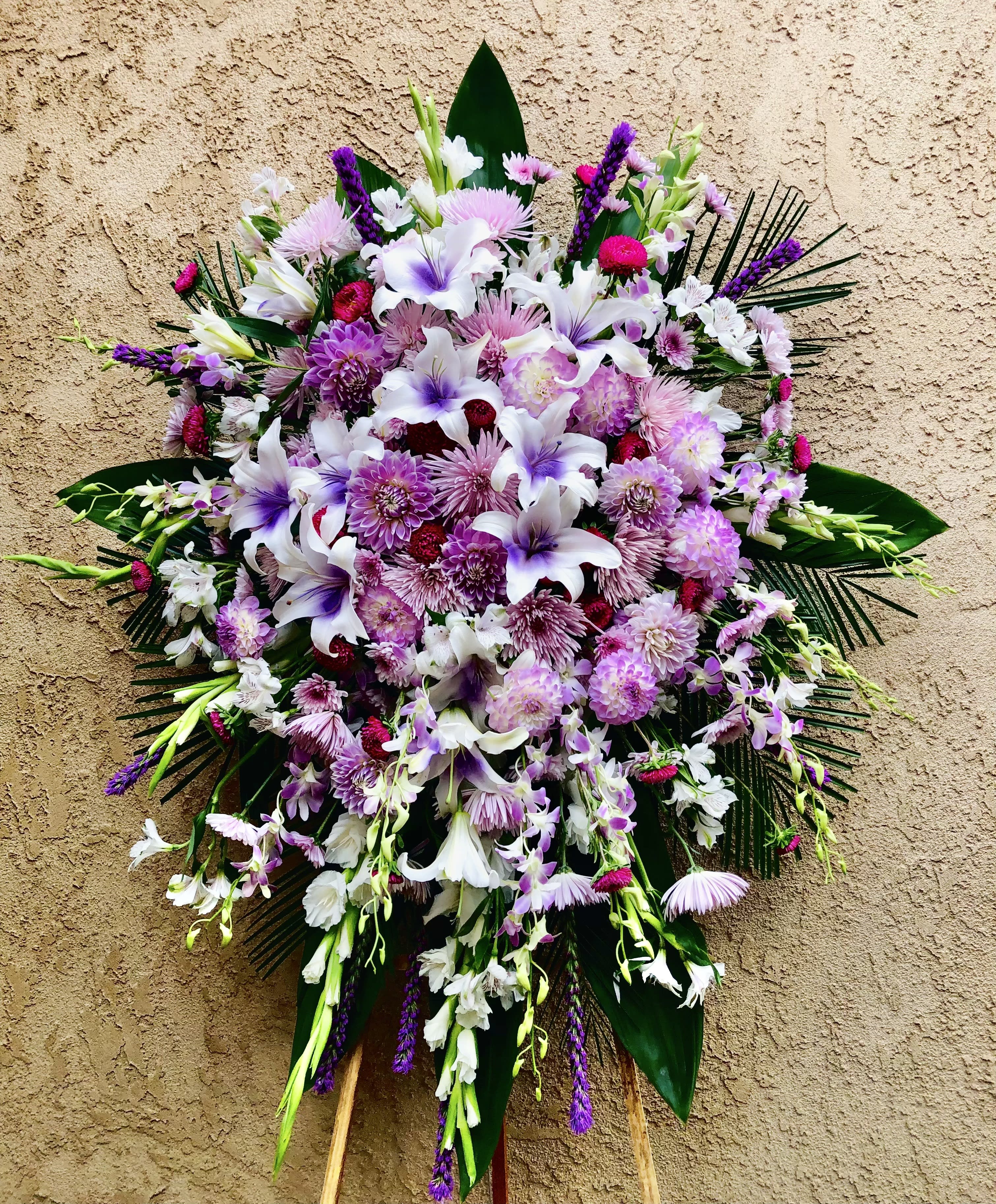 Lingering Lilacs - Beautiful standing spray arrangement with mixed purples, whites, and greens. Featuring lilies, mums, chrysanthemums, gladius, orchids, and leaf accents. 
