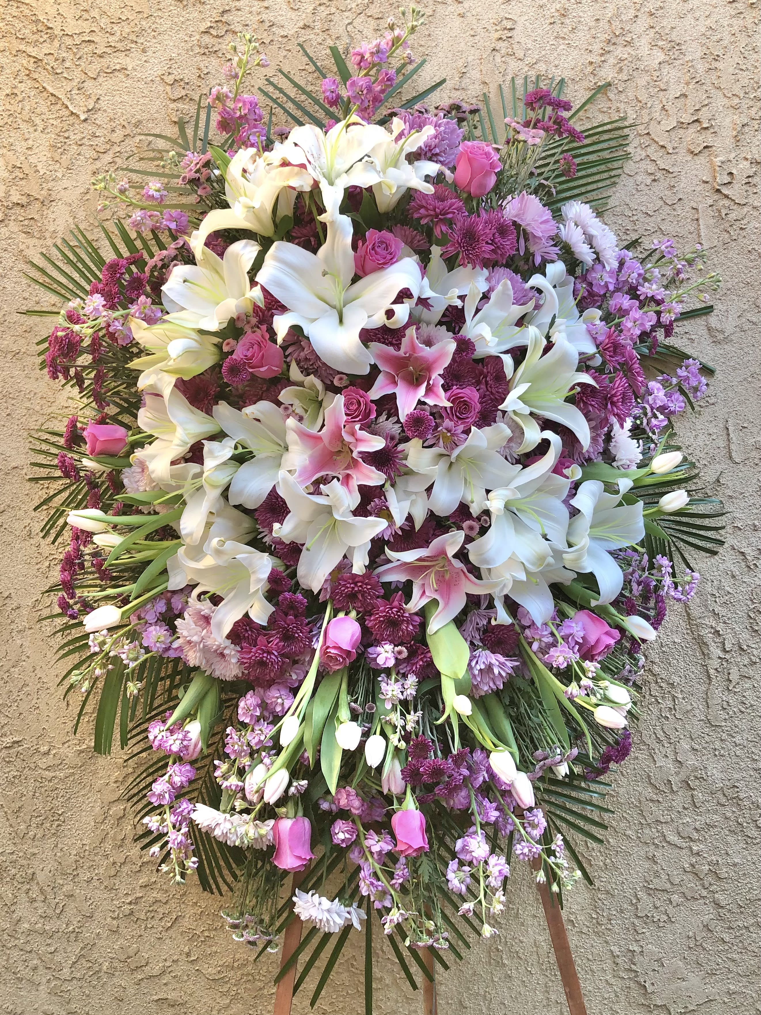 Lovely Memories - Beautiful standing funeral spray arrangement with a mix of purple, white, pink, and fushia flowers with green accents. Featuring lilies, mums, roses, tulips, stock, and green leaves.