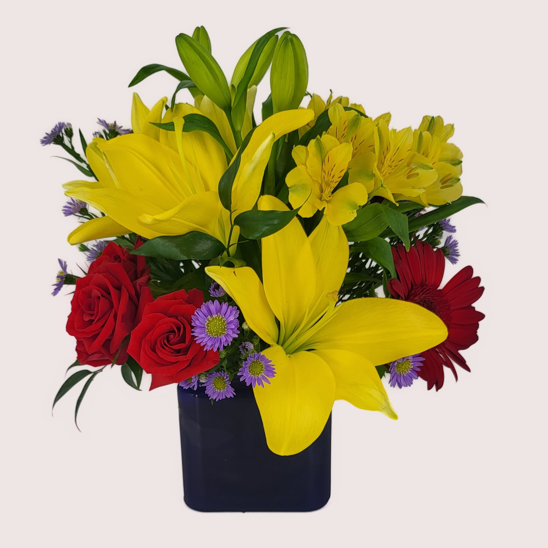 Blue Caribbean - The exciting bouquet includes yellow Asiatic lilies, red miniature gerberas, purple Matsumoto asters, red spray roses and yellow alstroemeria accented with fresh greenery. Delivered in a blue contemporary glass cube vase. Approximately 13&quot; W x 14&quot; H. 