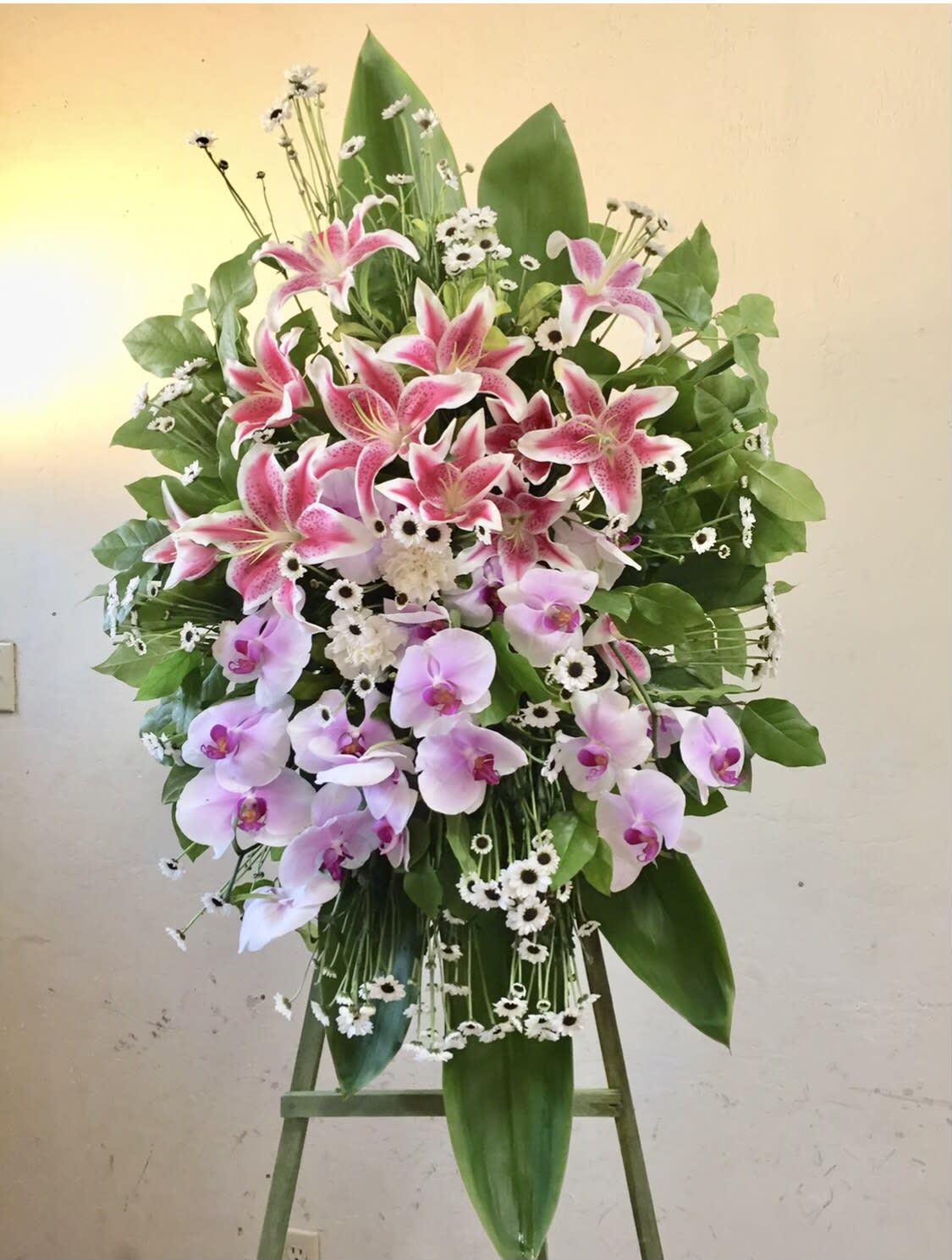 Sprouts of Love - Beautiful standing funeral spray of pink and lavender flowers with green and white accents. featuring lilies, orchids, daises and leaf accents. 
