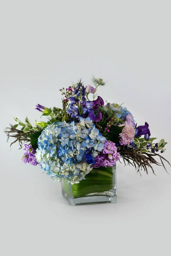 Lavender Blue Cube - 5&quot; sq cube leaf lined and filled with blue hydrangea, lavender stock, blue delphinium and a mix of seasonal  accent flowers.