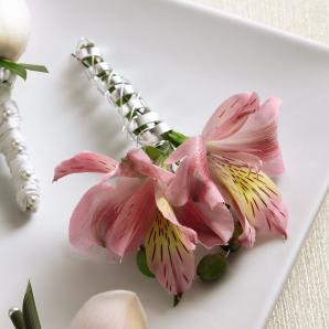 Pink Peruvian Lily Boutonniere Pink Peruvian Lily Boutonniere - The Pink Peruvian Lily Boutonniere adds a colorful flair to your wedding party. Beautiful Peruvian Lily blooms are brought together with green hypericum berries and tied together with a silver metallic wire for simply stylish look. Approx. 4âH x 2âW.