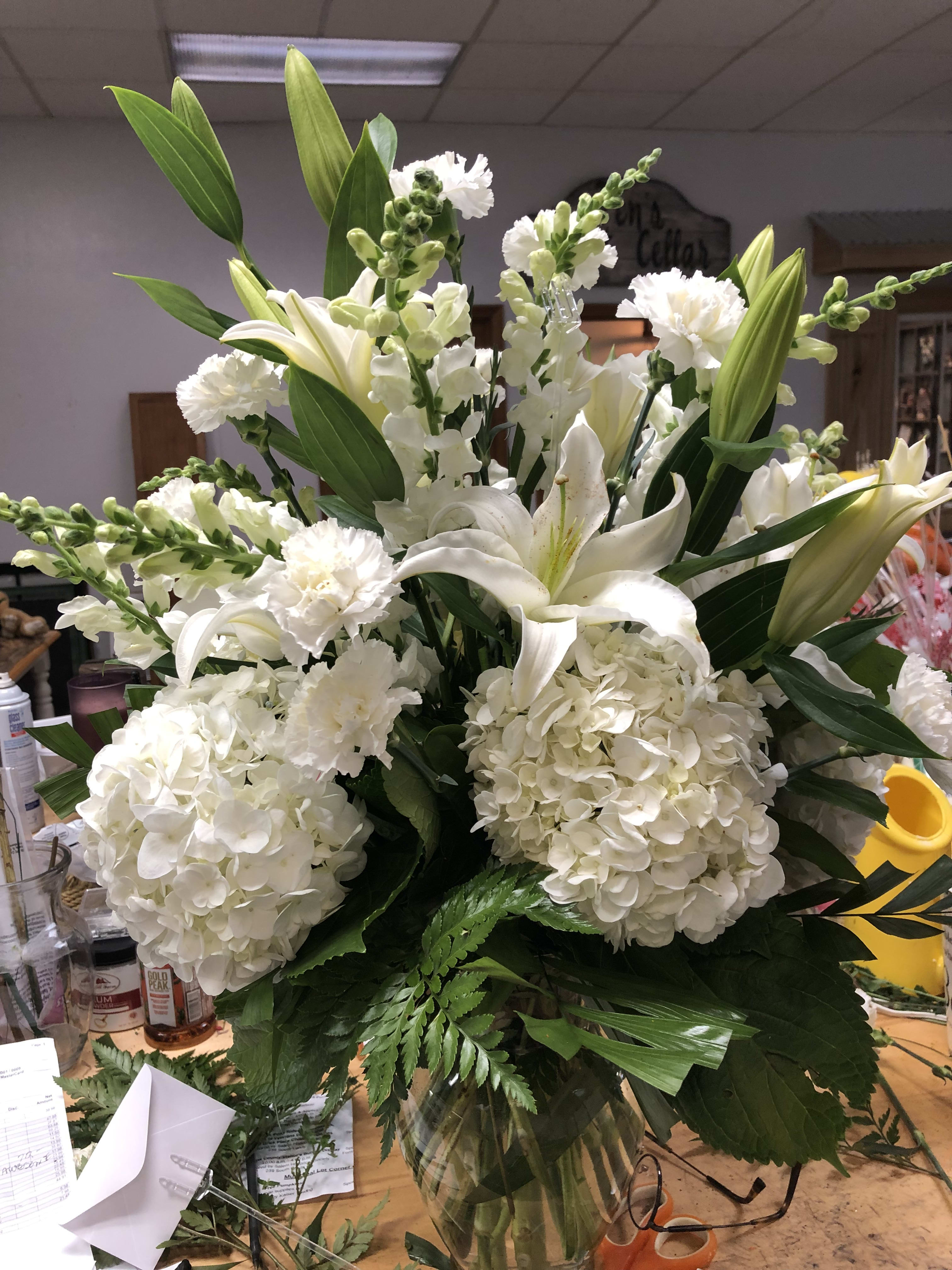 Your Majesty Your Majesty - White florals that include, hydrangea, lilies, roses snap dragons, roses in lushes greens that support it's majestic splendor.