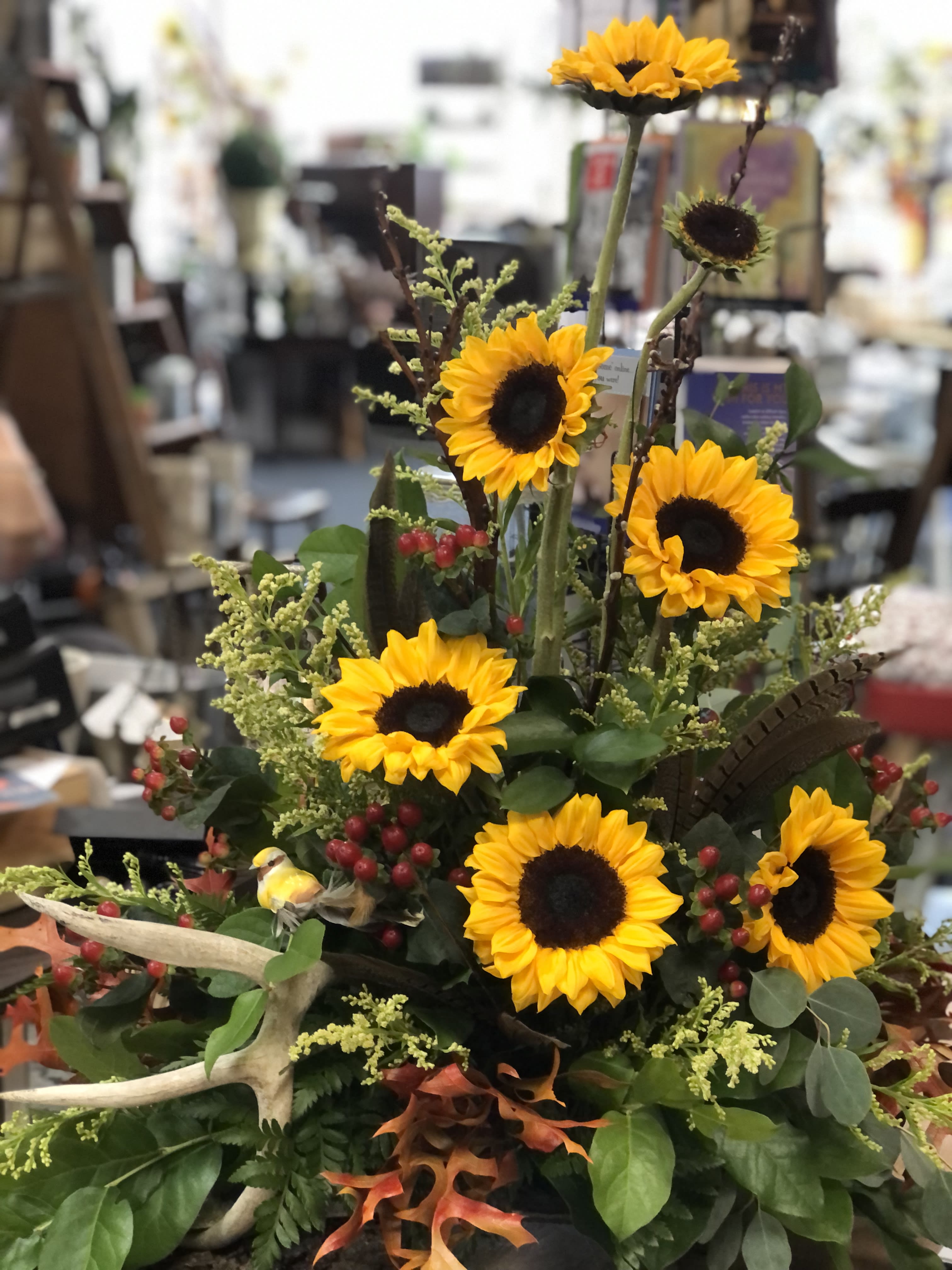 Monte - Yellow sunflowers, hypericum berries, solidago aster, dried leaves placed on a slab of bark wood with a deer horn. These specialty arrangements are our specialty. We can honor your loved one in many ways that will reflect is personality.