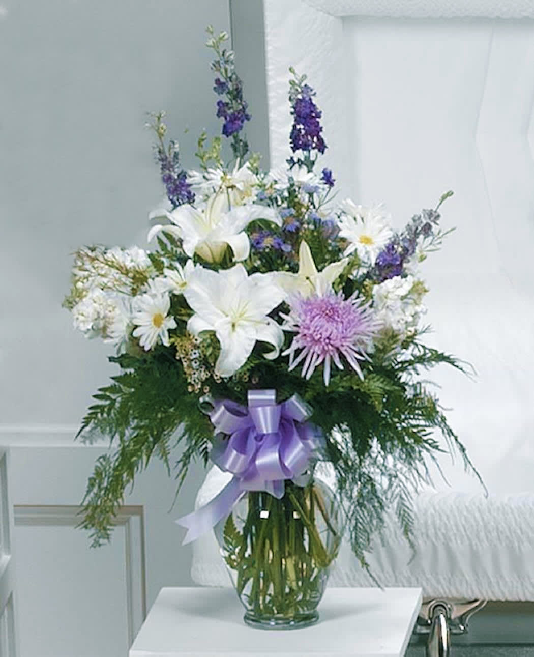 Pure Granduer - A stunning display of whites and lavender mums, lilies, stock and larkspur complimenting with beautiful greenery.