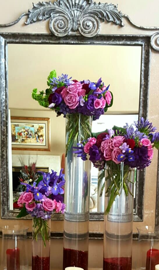 TRIPLE LADIES - CLUSTERS OF BUBBLE GUM PINK ROSES, IRIS, AND RICH PURPLE HUES. WITH A DRASTIC BURST OF GREEN BELLS OF IRELAND. THESE STATEMENT PIECES WILL ENHANCE THE ATMOSPHERE OF ANY EVENT.