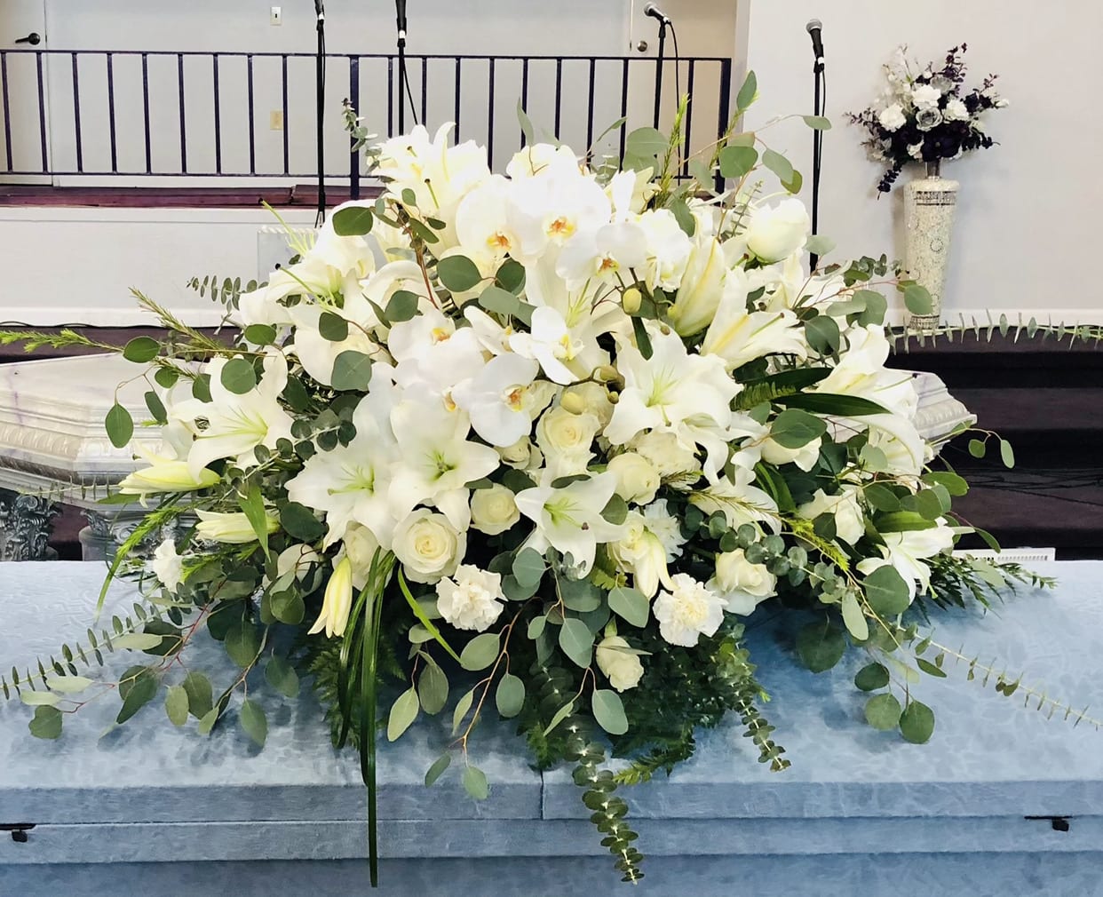 Casket 6 - Beautiful and elegant white casket arrangement featuring lilies, orchids, roses, carnations, and green accents.