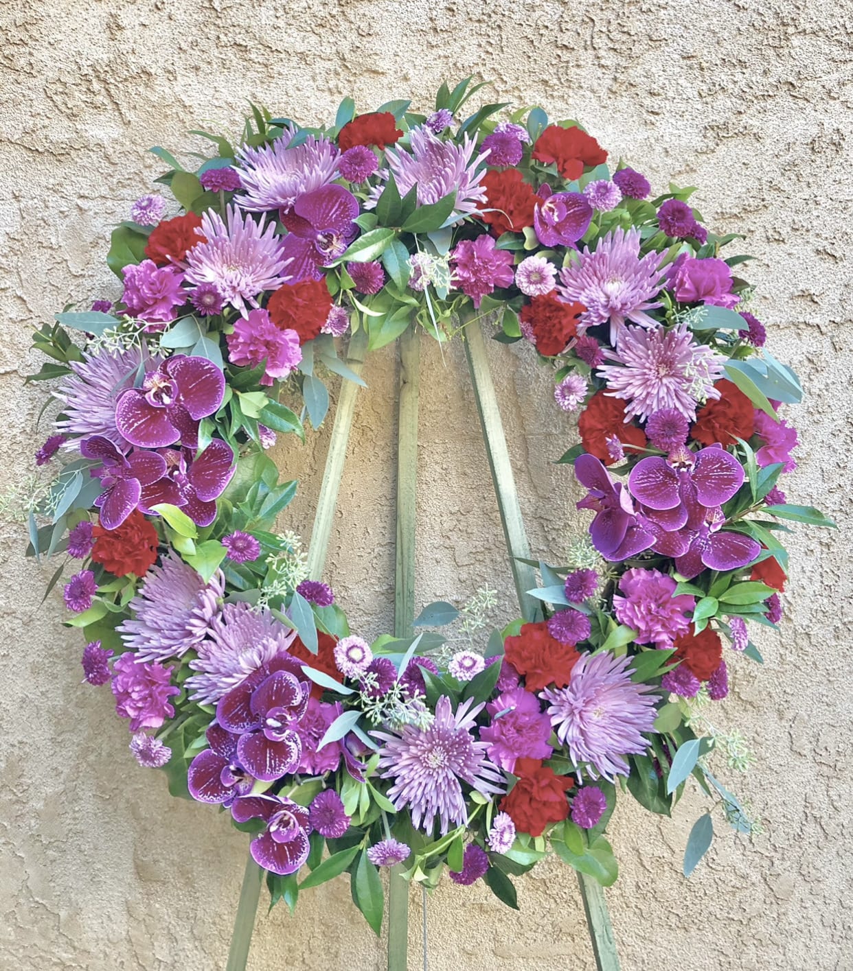 Locks of Violet - Beautiful violet and red standing funeral spray flowers featuring mums, orchids, daises, carnations, and green accents.