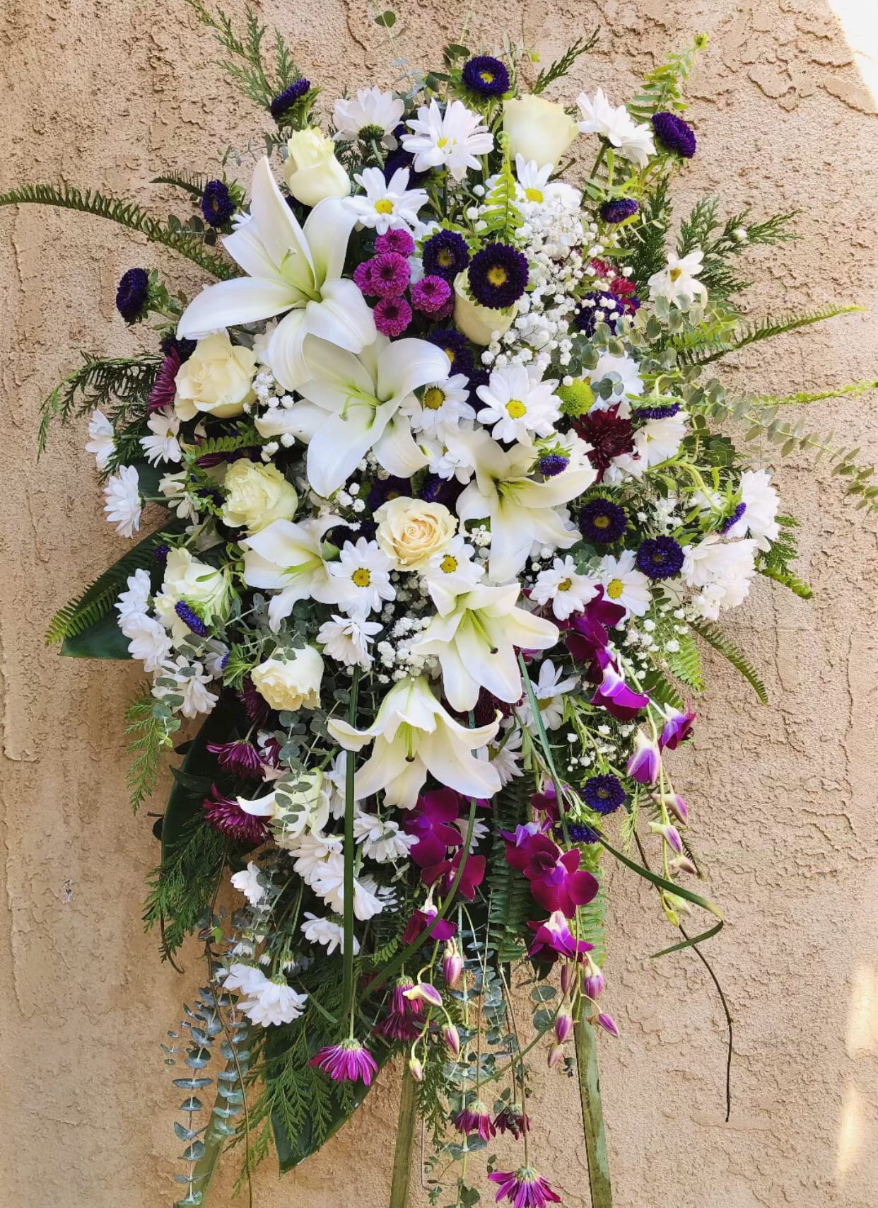 Spring's Memory - Beautiful purple and white standing funeral spray arrangement featuring daises, lilies, dahlias, roses, orchids, and green accents.