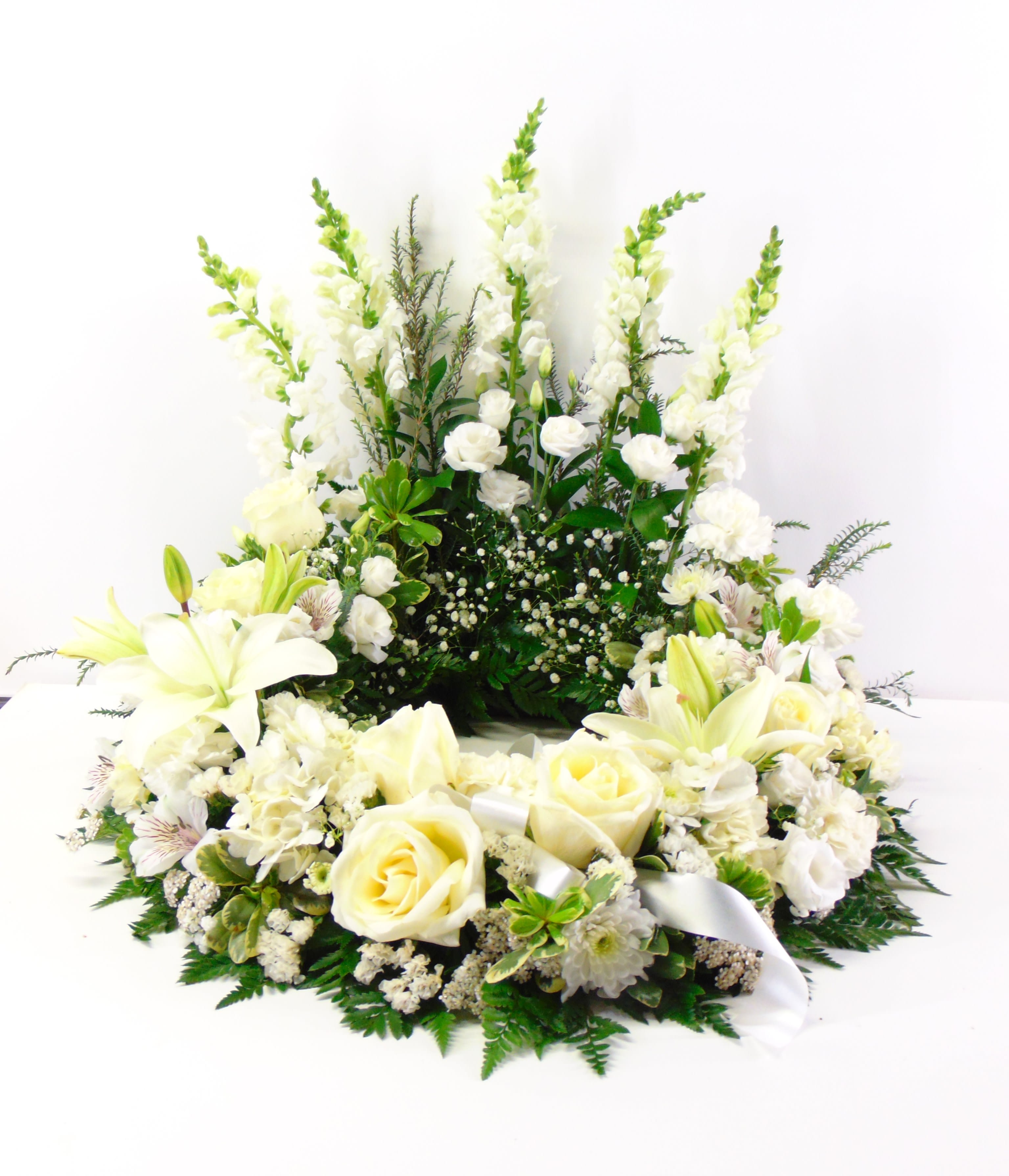 Heaven Scent Cremation Wreath - A Heavenly white embrace of scented white roses, hydrangea, lilies, snapdragon fragrant lisianthus, carnations, alstromeria and baby's breath. Standard option is pictured. The deluxe and premium option will feature more snapdragons coming down the sides and more roses around the front and one more lily bloom.
