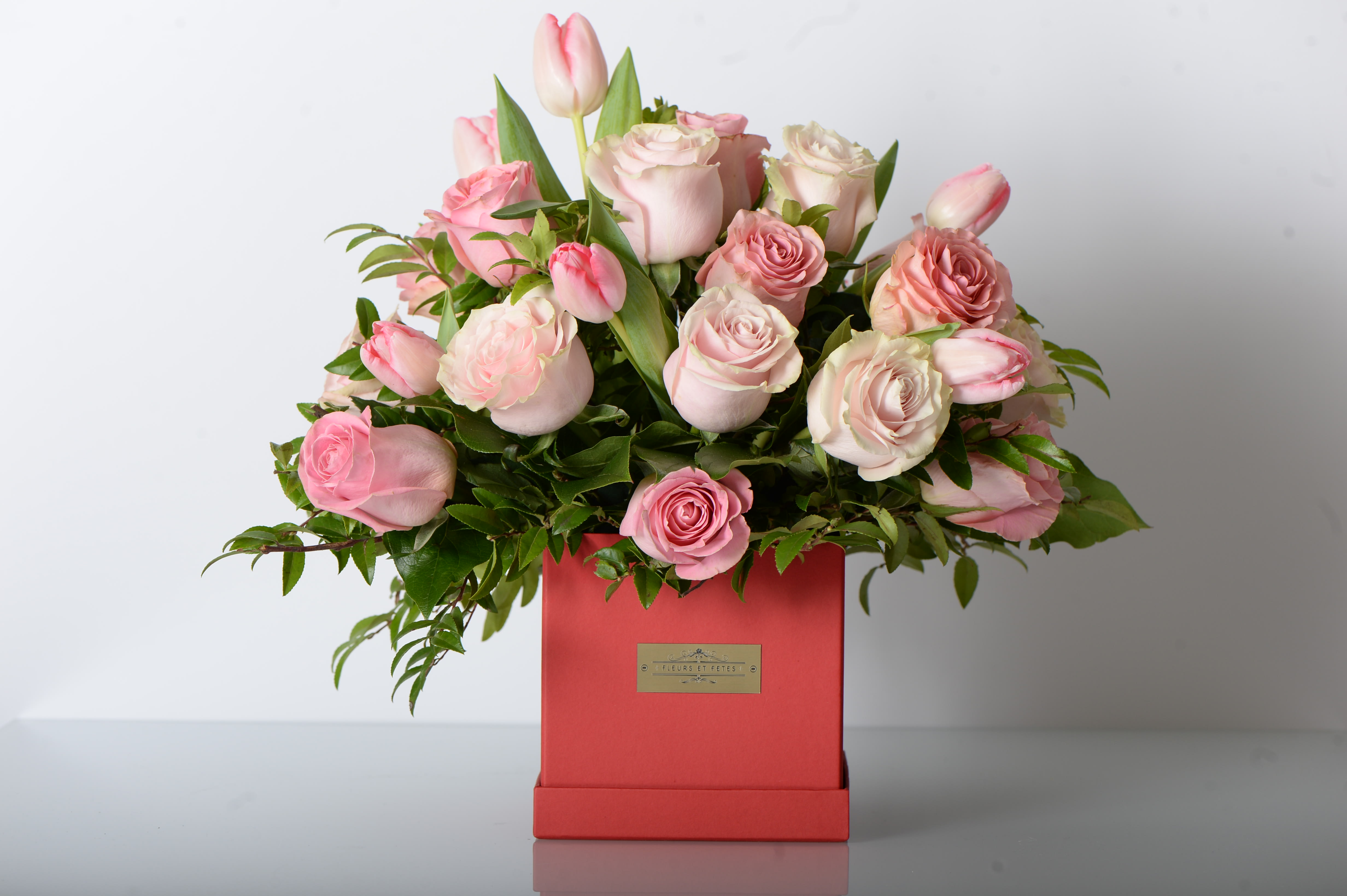 Passion - The soft tone of pink roses and tulips combined with lemon leaves arranged in our small red signature box.