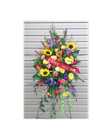 Beautiful Spirit Spray - This standing spray includes Sunflowers, Iris, pink Carnations, red and yellow Roses, yellow Gerber Daisies and pink Snap Dragons. Also includes a ribbon that can be customized to say a few words of your choice.   All flowers and colors are subject to change due to availability.    FCF-0310