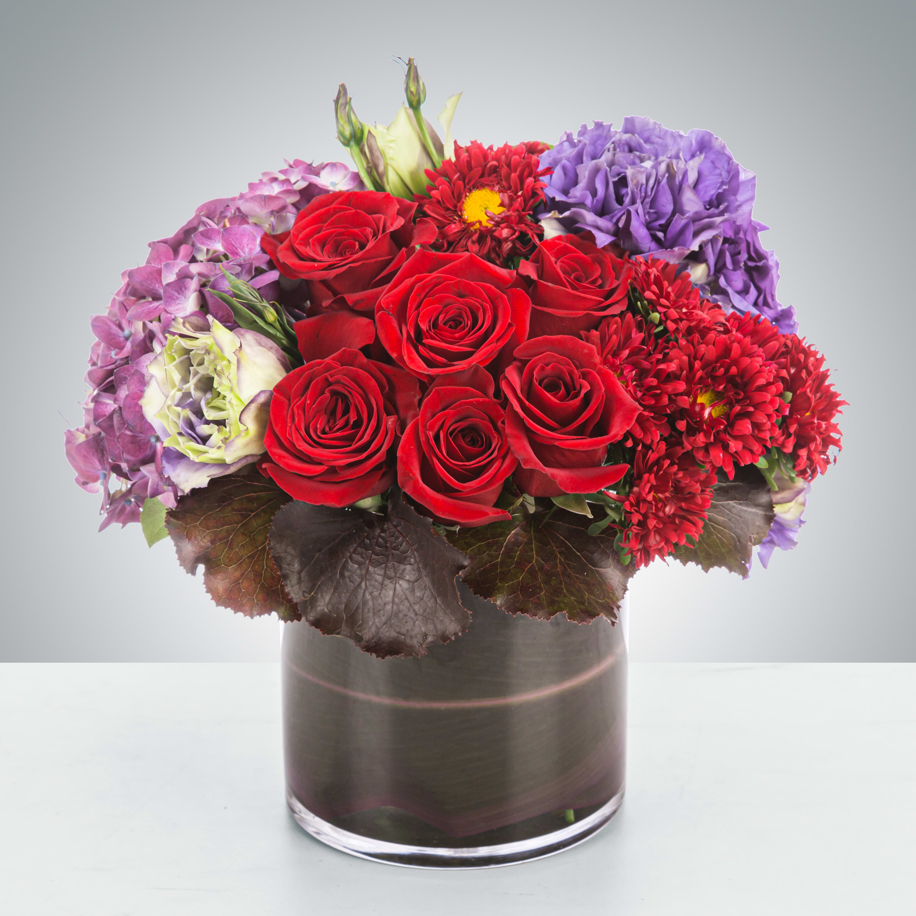 Garnet - This deep jewel tone arrangement featuring red roses, purple hydrangea and purple lisianthus is a dream. Garnets symbolize higher thinking and are the birthstone for January making this a great wintertime birthday present, thank you, anniversary or congratulations, Valentin's Day, for an academic or career win.   Approximate Dimensions: 11&quot;D x 11&quot;H
