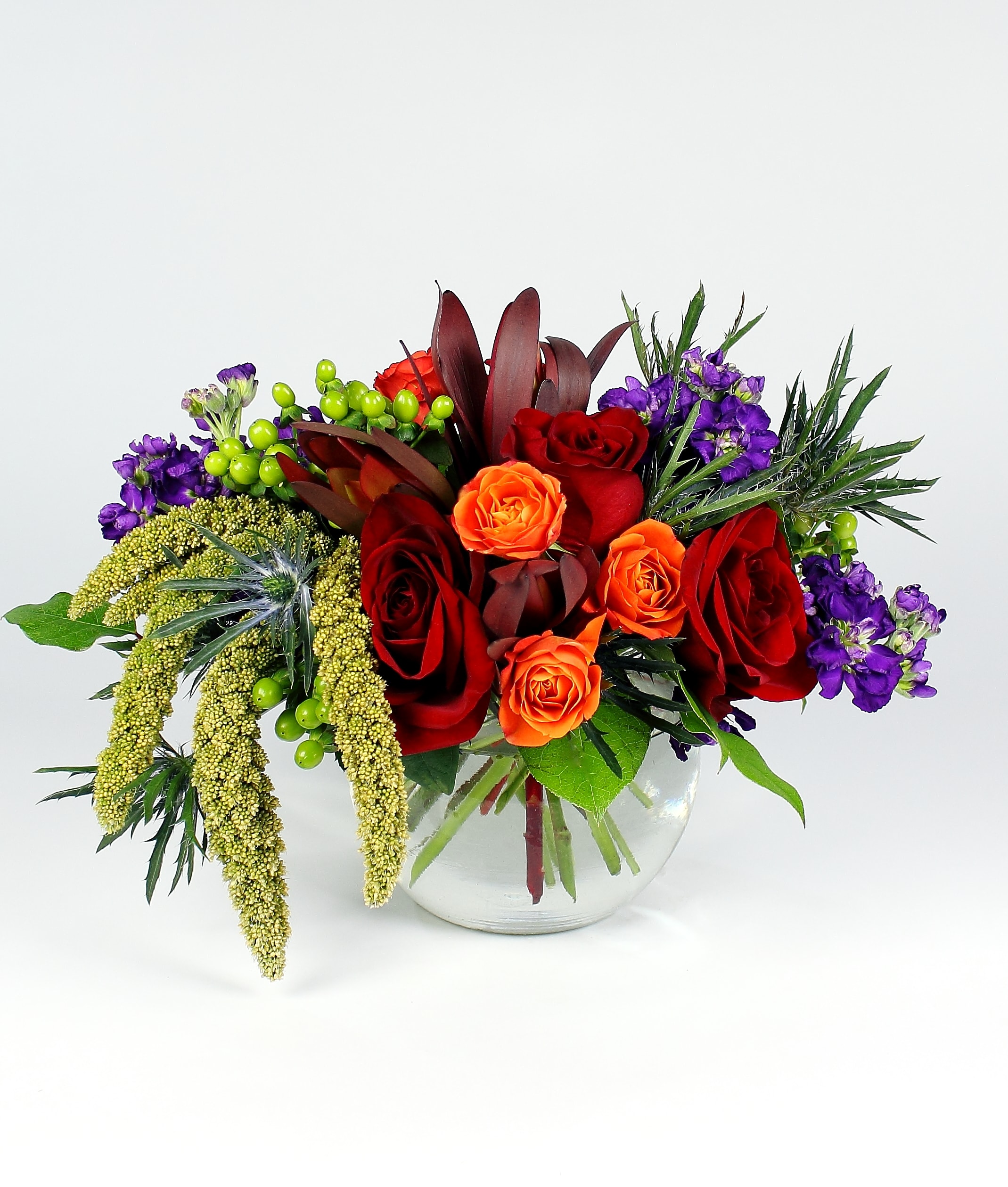 DEEP VELVET BLOSSOMS DEEP VELVET BLOSSOMS - This classic glass bubble bowl is over flowing with texture. A mix of velvety red roses and dark purple stock is accented by crisp thistle and leathery leucadendron. Topped off with hanging millet (Fresh or Dried) and bright spray roses. You'll just have to feel it to believe it! Approx, 13" by 9". *Due to availability, on occasion it may be necessary to substitute a certain flower or container for your order.