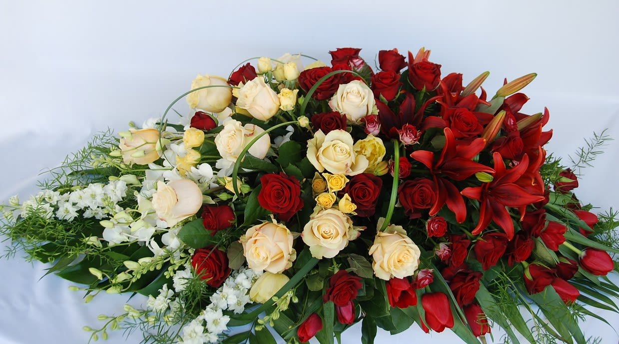Garden of Grandeur Casket Spray  - This casket arrangement has rich red lilies, tulips, roses, and spray roses contrasting with white orchids, larkspur, ivory roses and spray roses. 